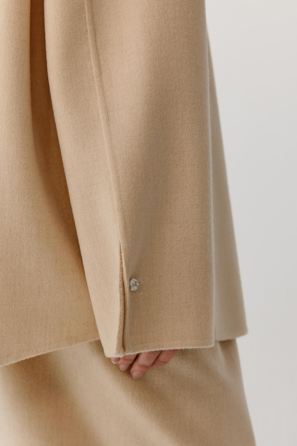 Close-up showing the side seam, hem and fluid drape of the beige melange double-face wool overshirt.