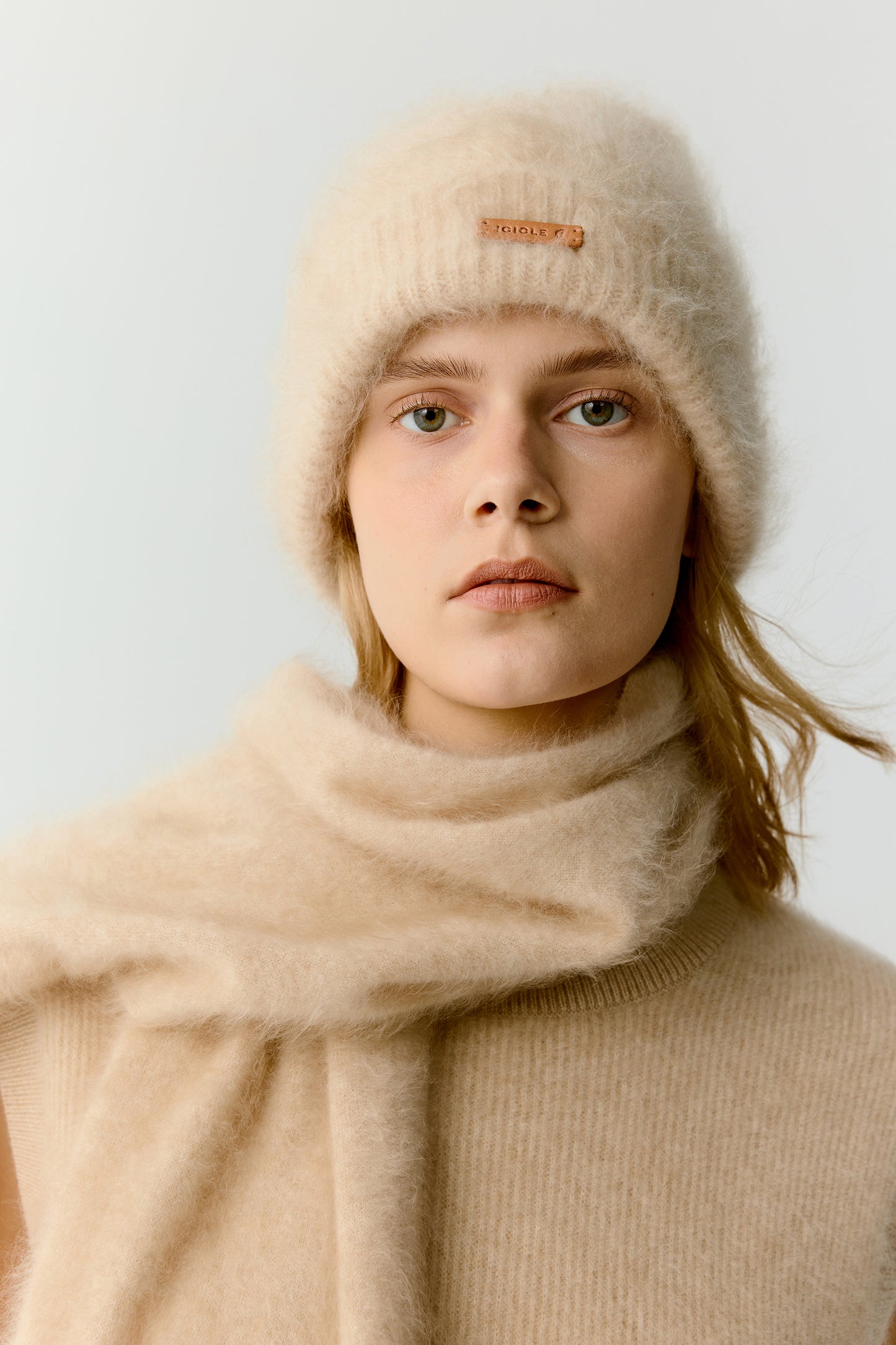 Woman wearing a beige knit beanie and matching scarf on a light background