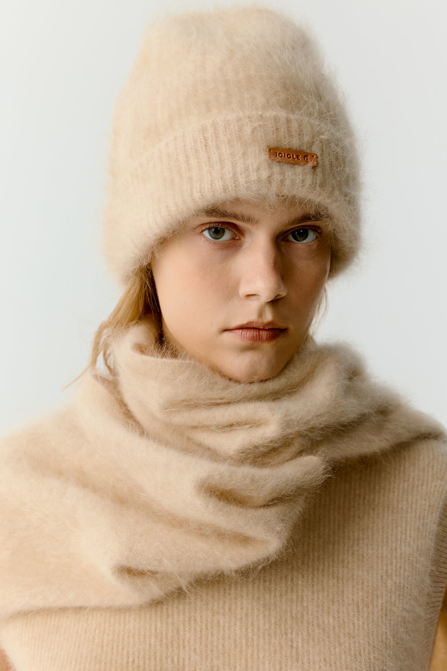 Front view of a woman wearing a beige knit beanie and scarf on a light background