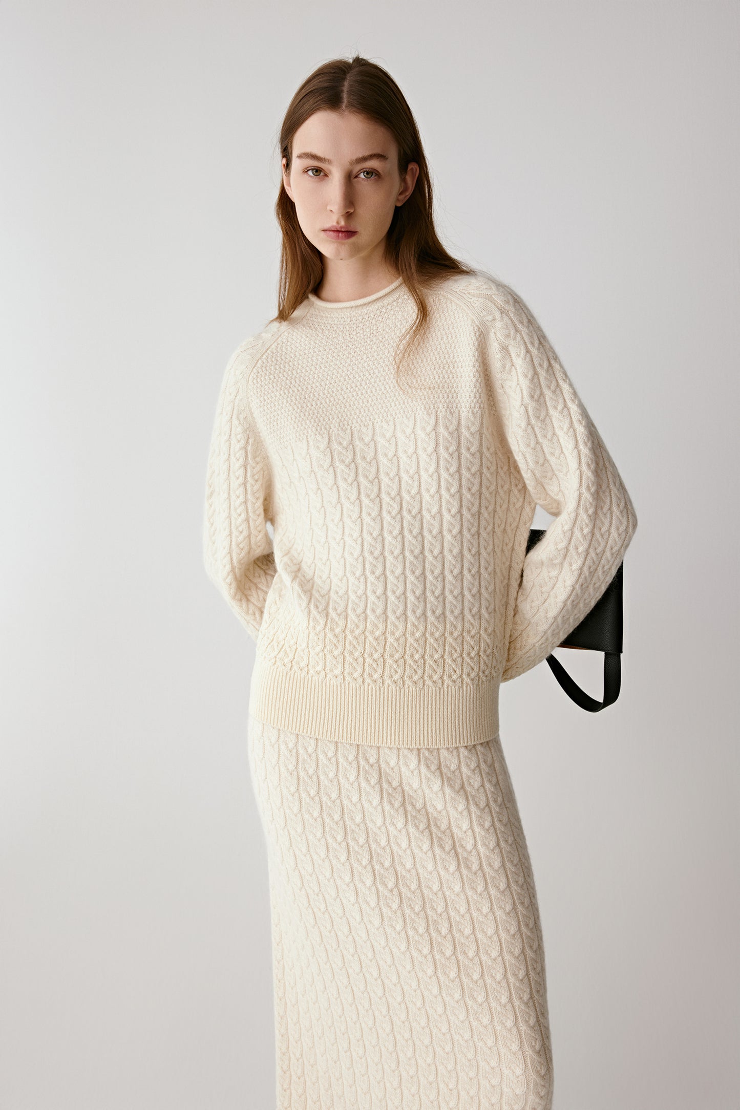 Front view of a model wearing a cream cable-knit cashmere jumper with a relaxed fit and long sleeves.