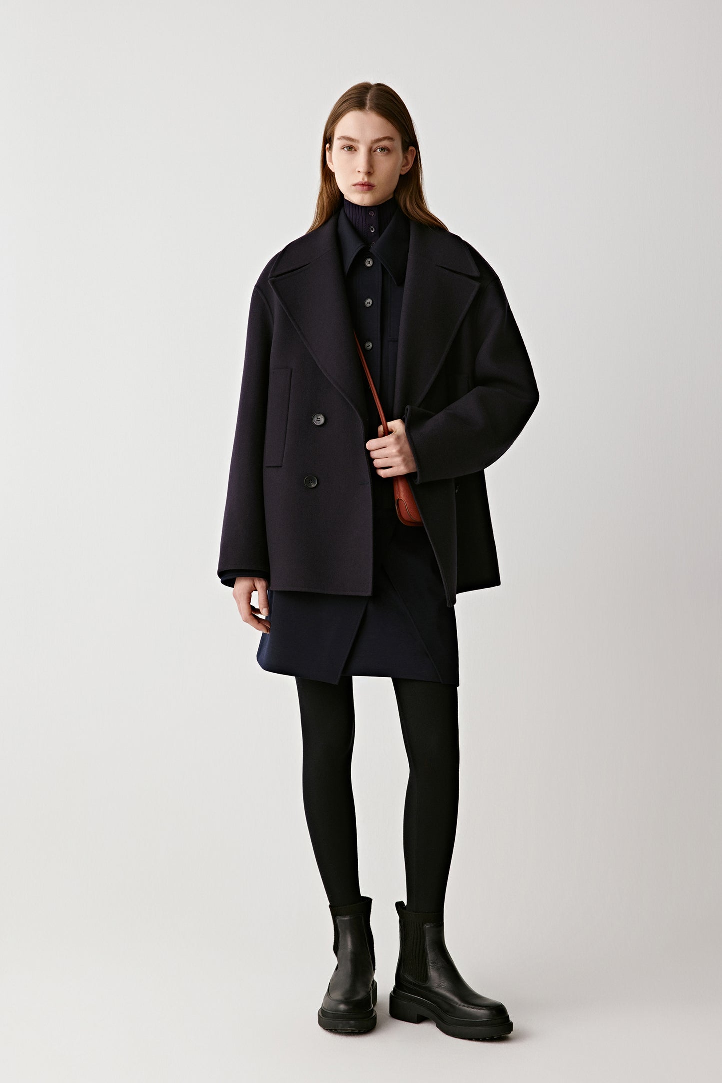 Front view of a model wearing a short double-faced wool and cashmere peacoat in navy, styled with clean lines and a double-breasted closure.