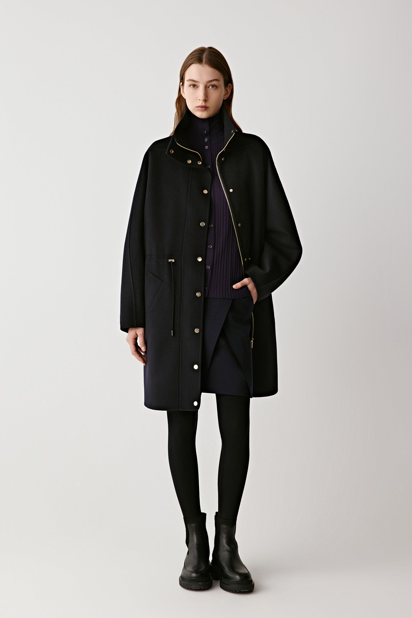 Front view of a model wearing a navy double-faced wool and silk coat with a structured stand collar and gold-tone press-stud fastening.