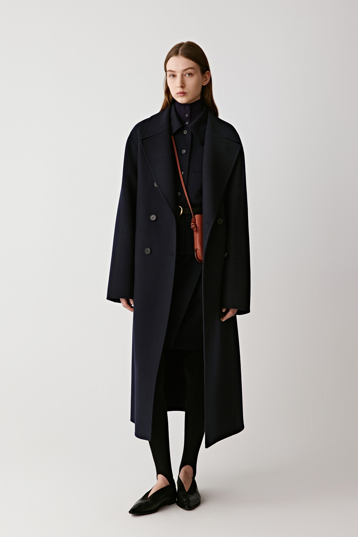 Front view of a model wearing a long navy double-faced wool and cashmere coat with clean lines and a double-breasted design.