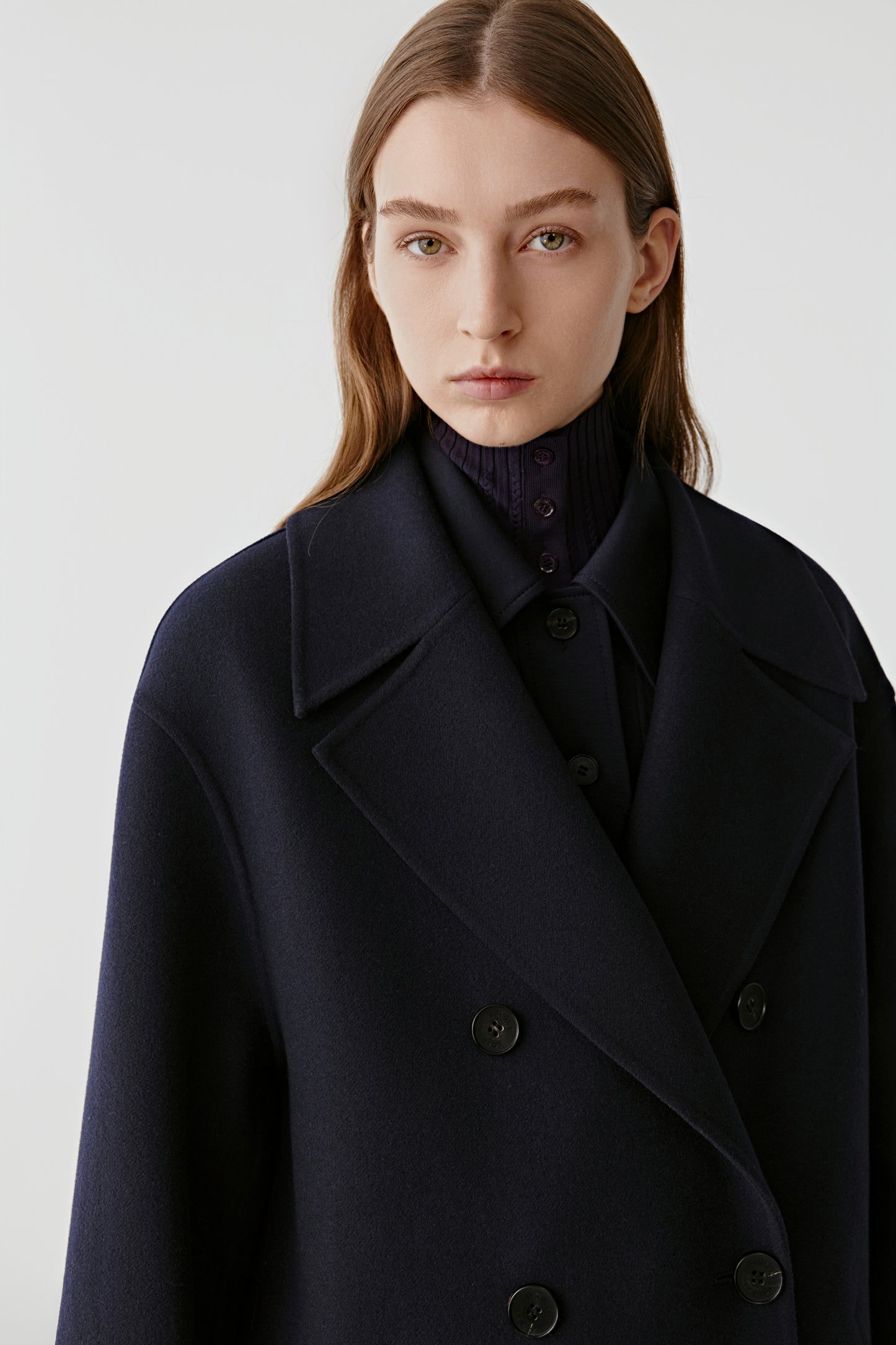Portrait view of the model wearing the navy wool and cashmere coat with wide lapels.