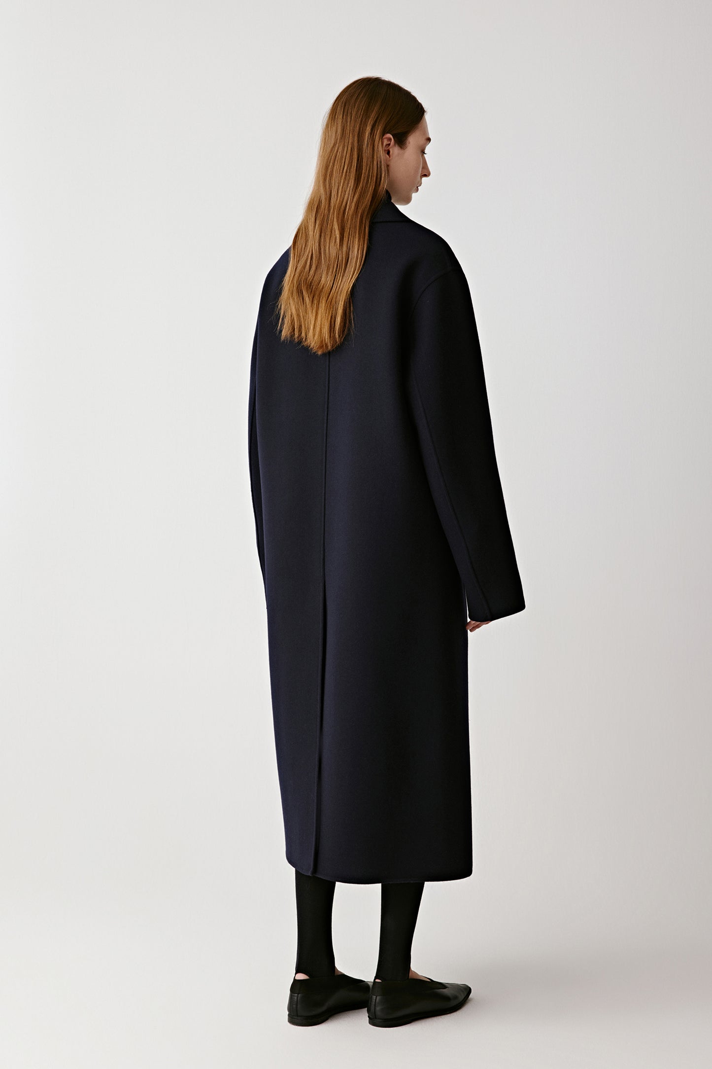 Back view of the navy coat showing its straight, refined drape.