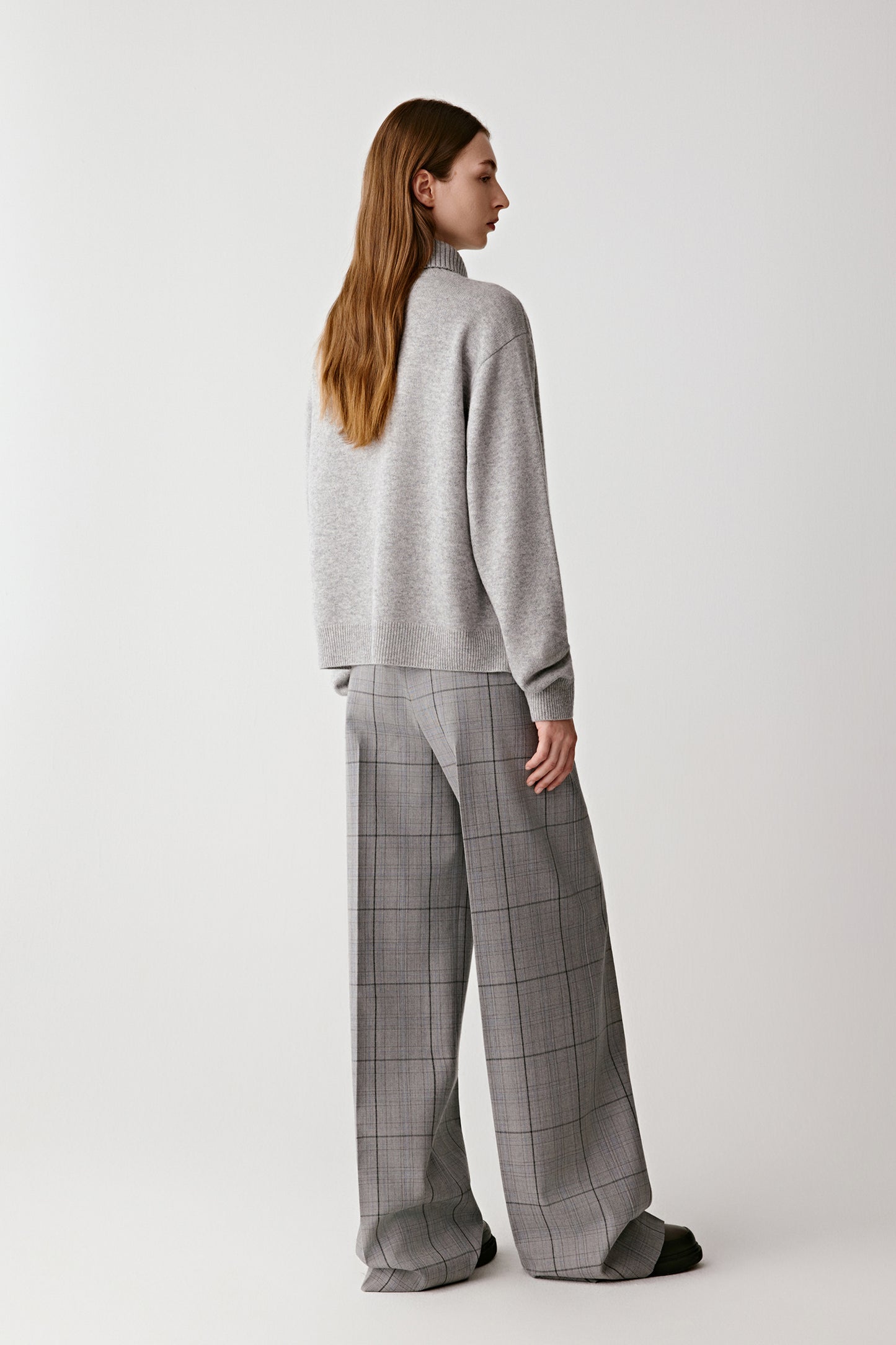Woman wearing a gray sweater and checked pants on a white background