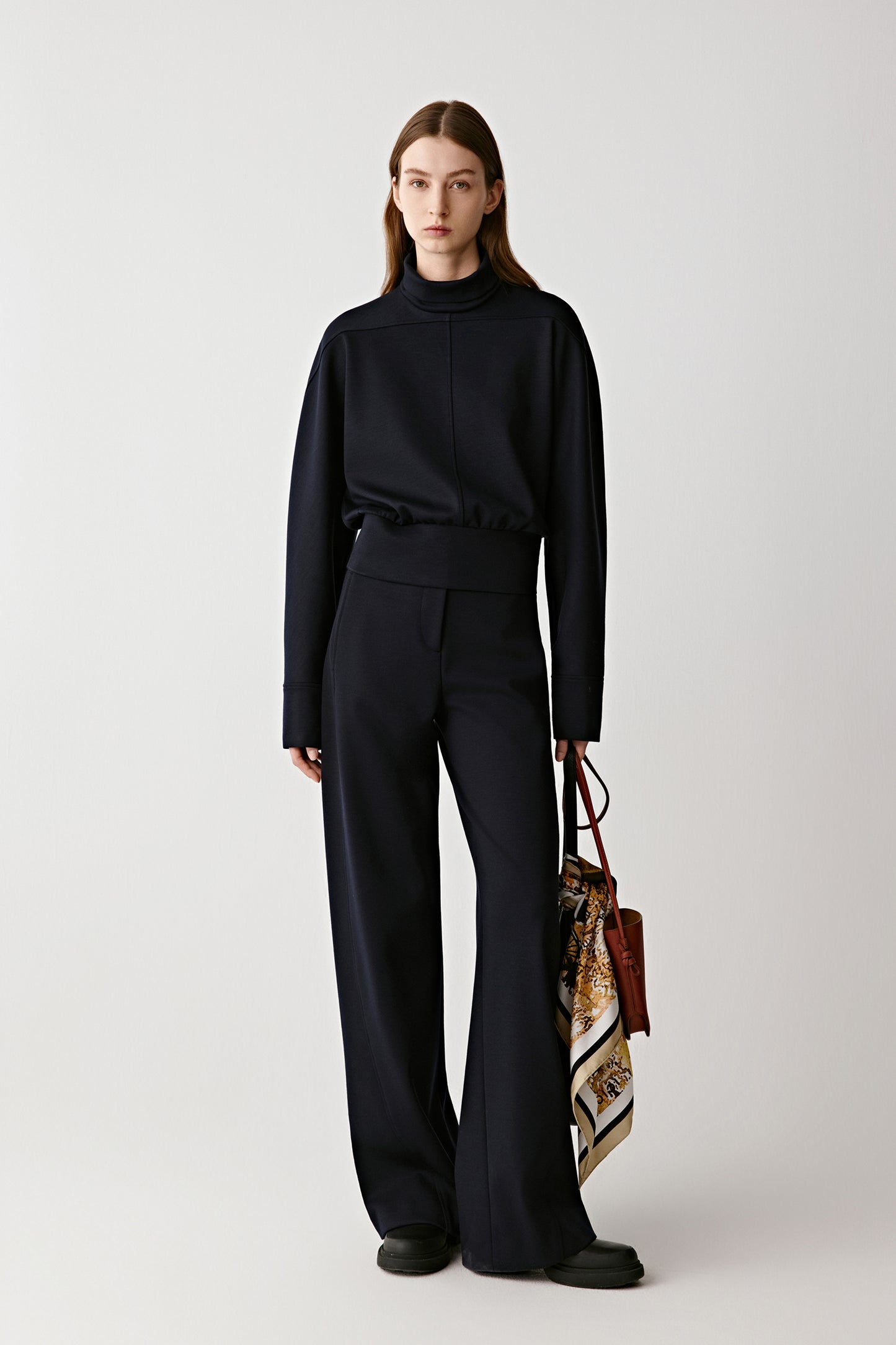 Woman wearing a black outfit holding a patterned handbag on a white background