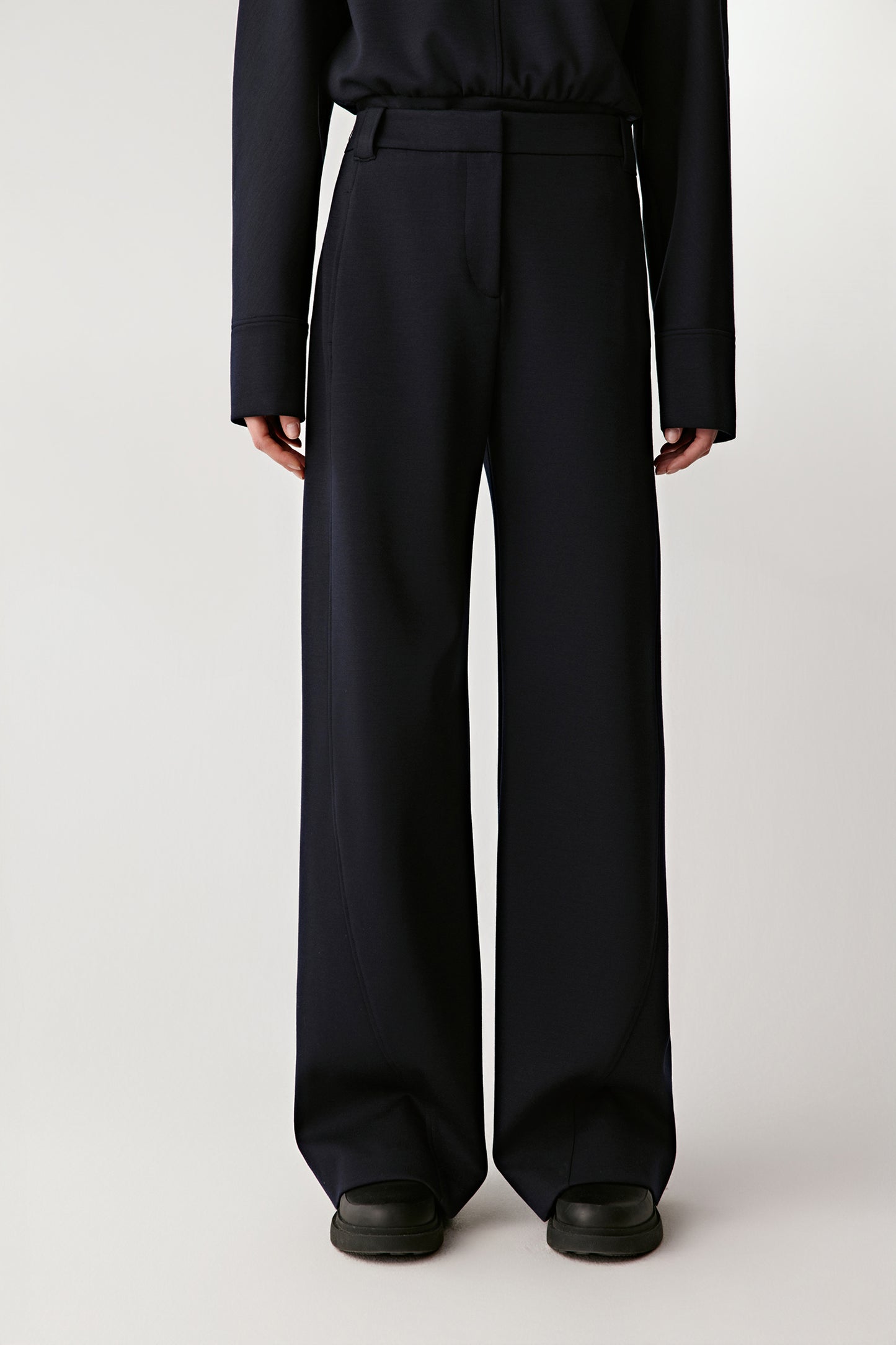 Person wearing black high-waisted pants and black shoes on a white background