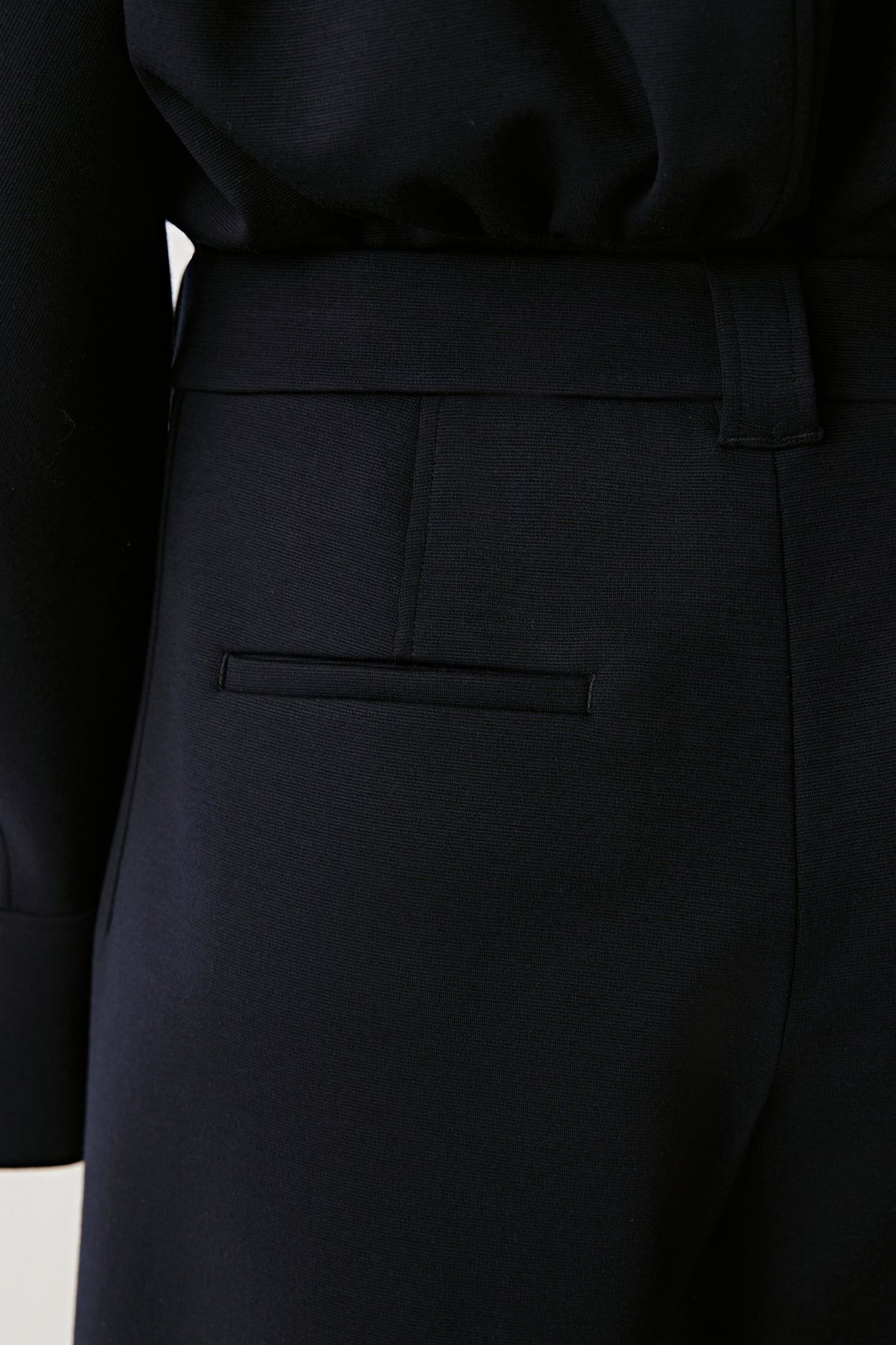 Close-up of a black coat with pocket detail on a light background