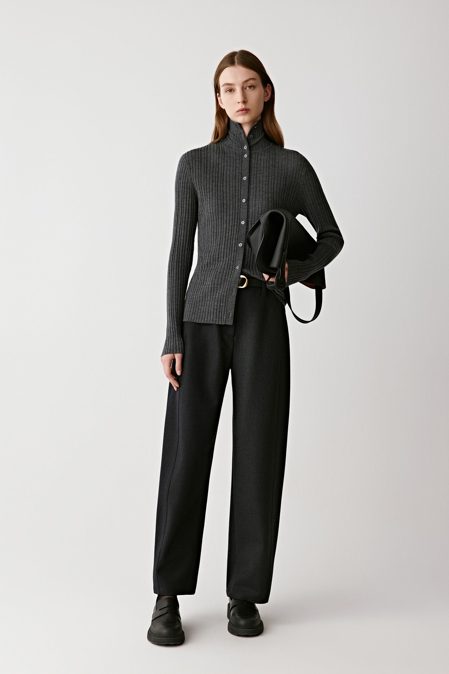 Front view of a woman wearing dark grey wool trousers with a high waist and clean straight leg.