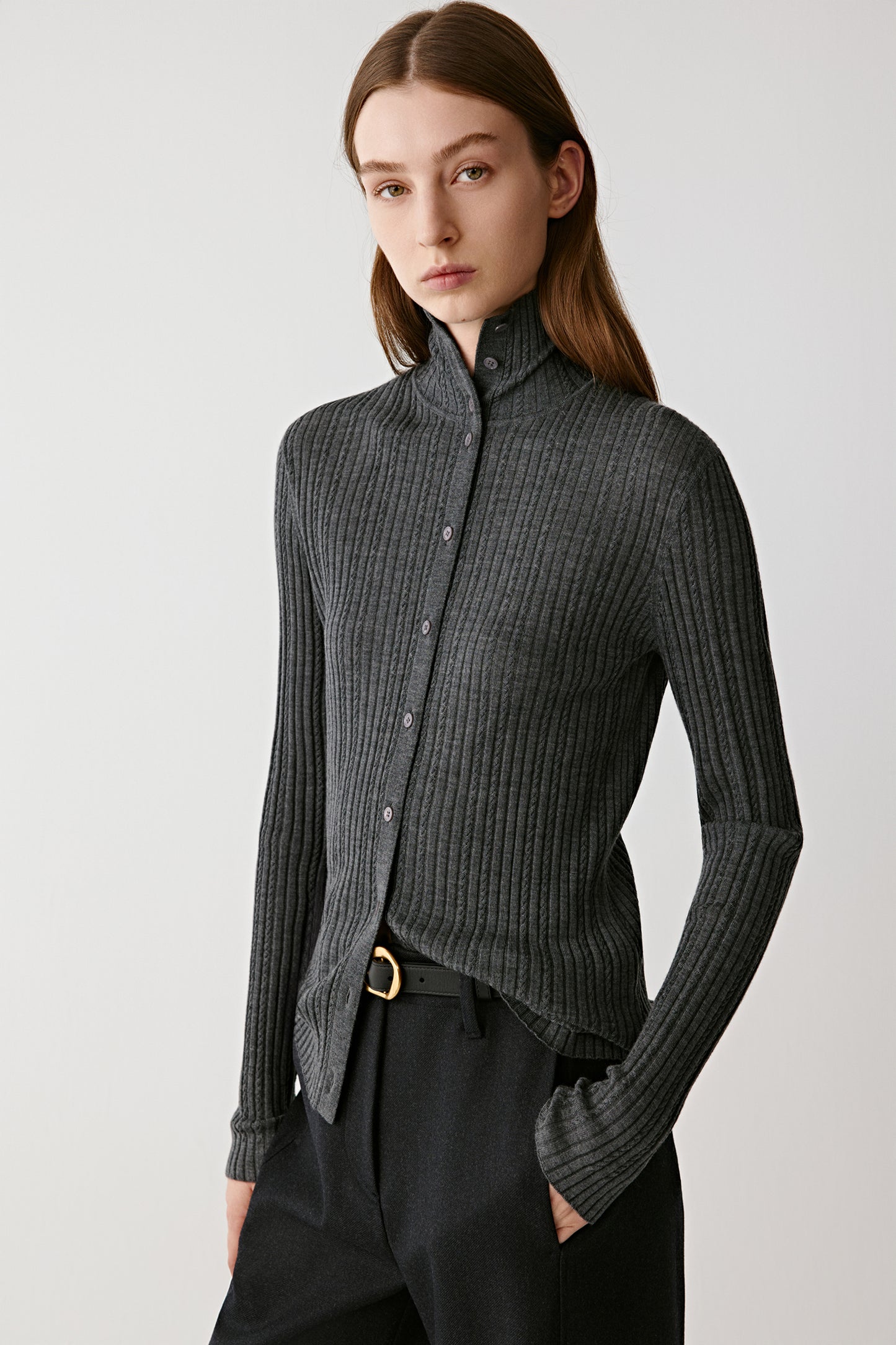 Front view of a model wearing a grey ribbed wool cardigan with a high neck and button placket.