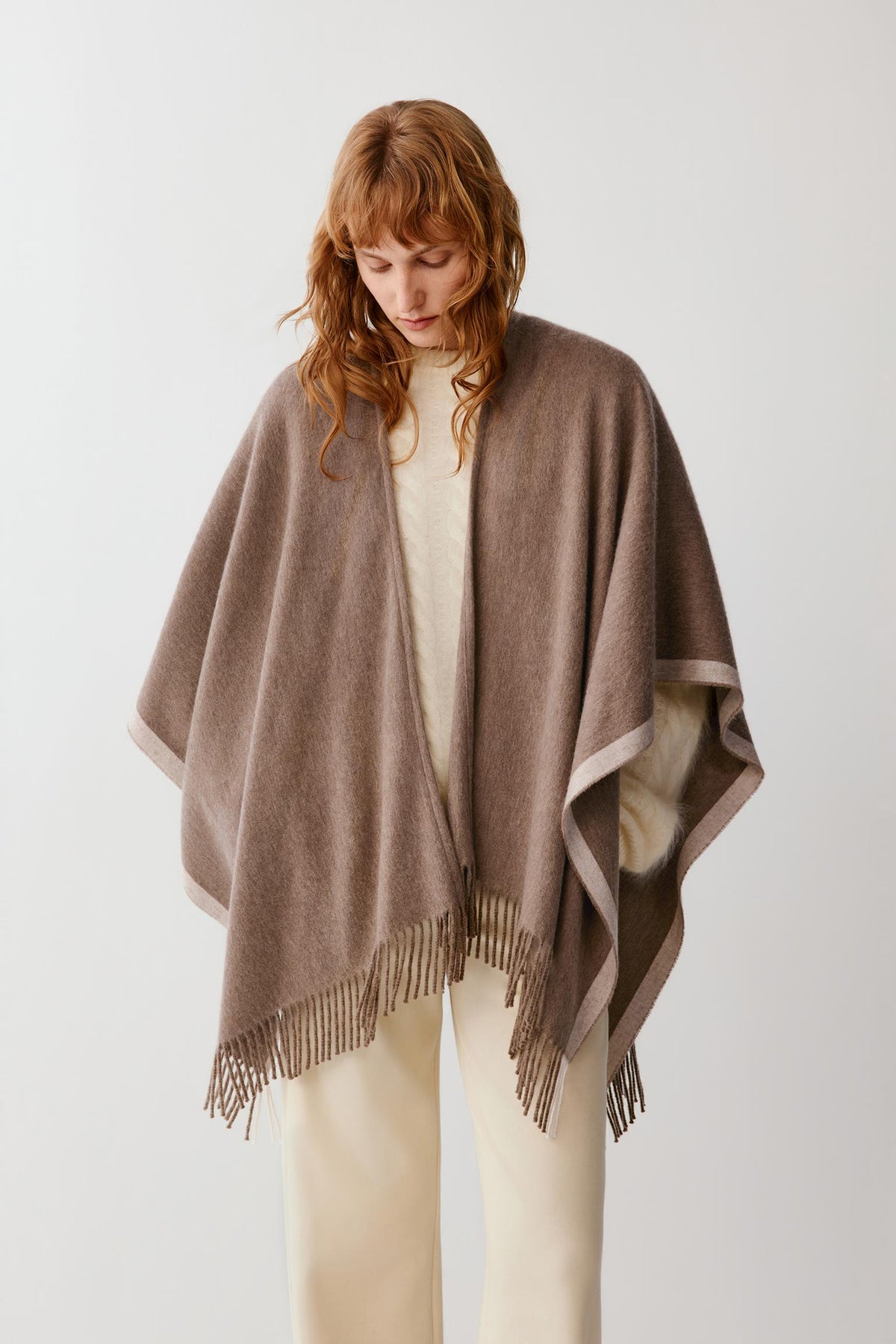 Side view of a woman wearing a brown cashmere shawl, highlighting the asymmetric drape and fringed trims.