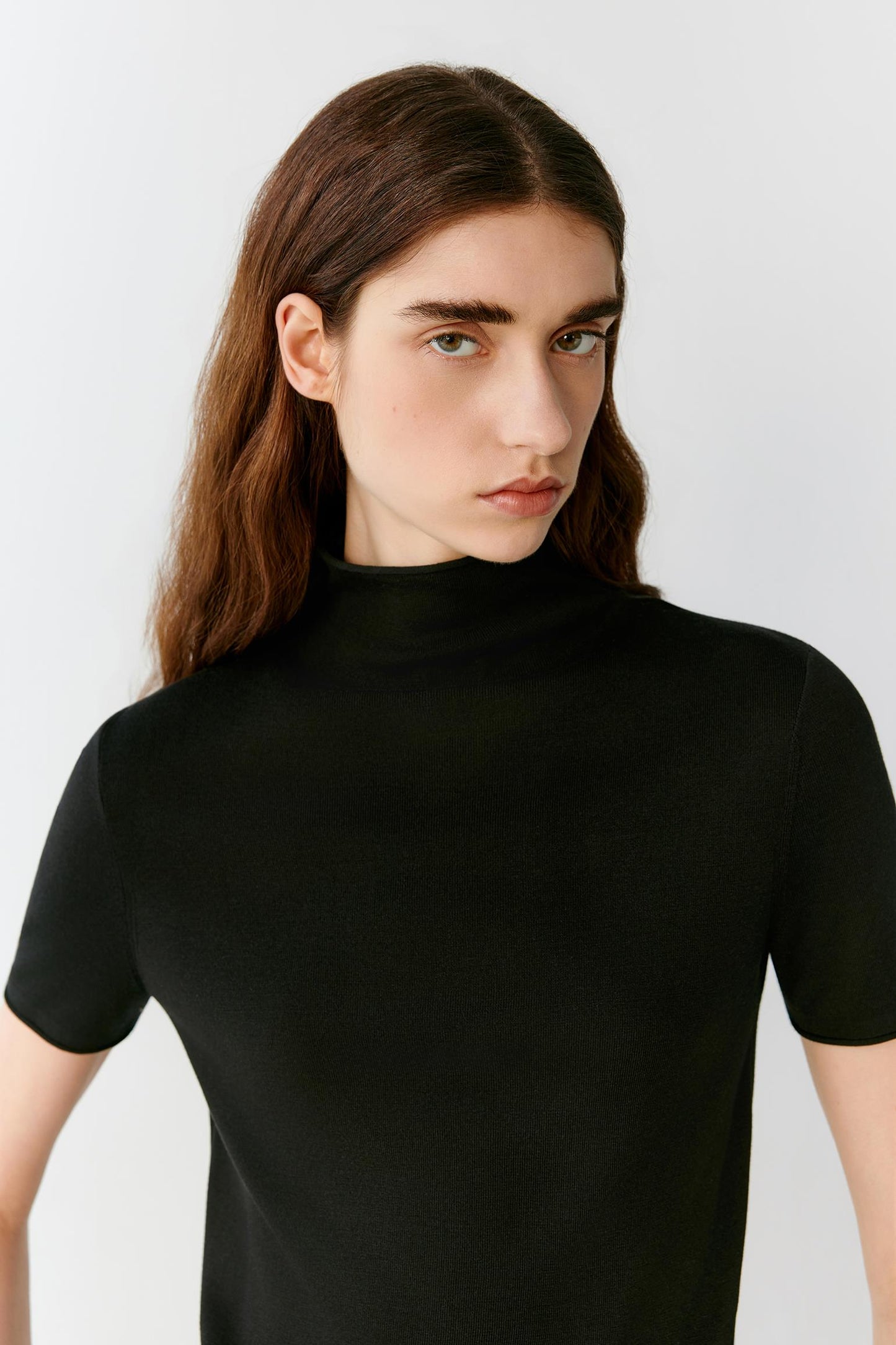 Close-up portrait focusing on the mock neckline, shoulders and upper body construction. The image reveals the smooth texture, compact knit structure and fine ribbed neckline that frame the silhouette.