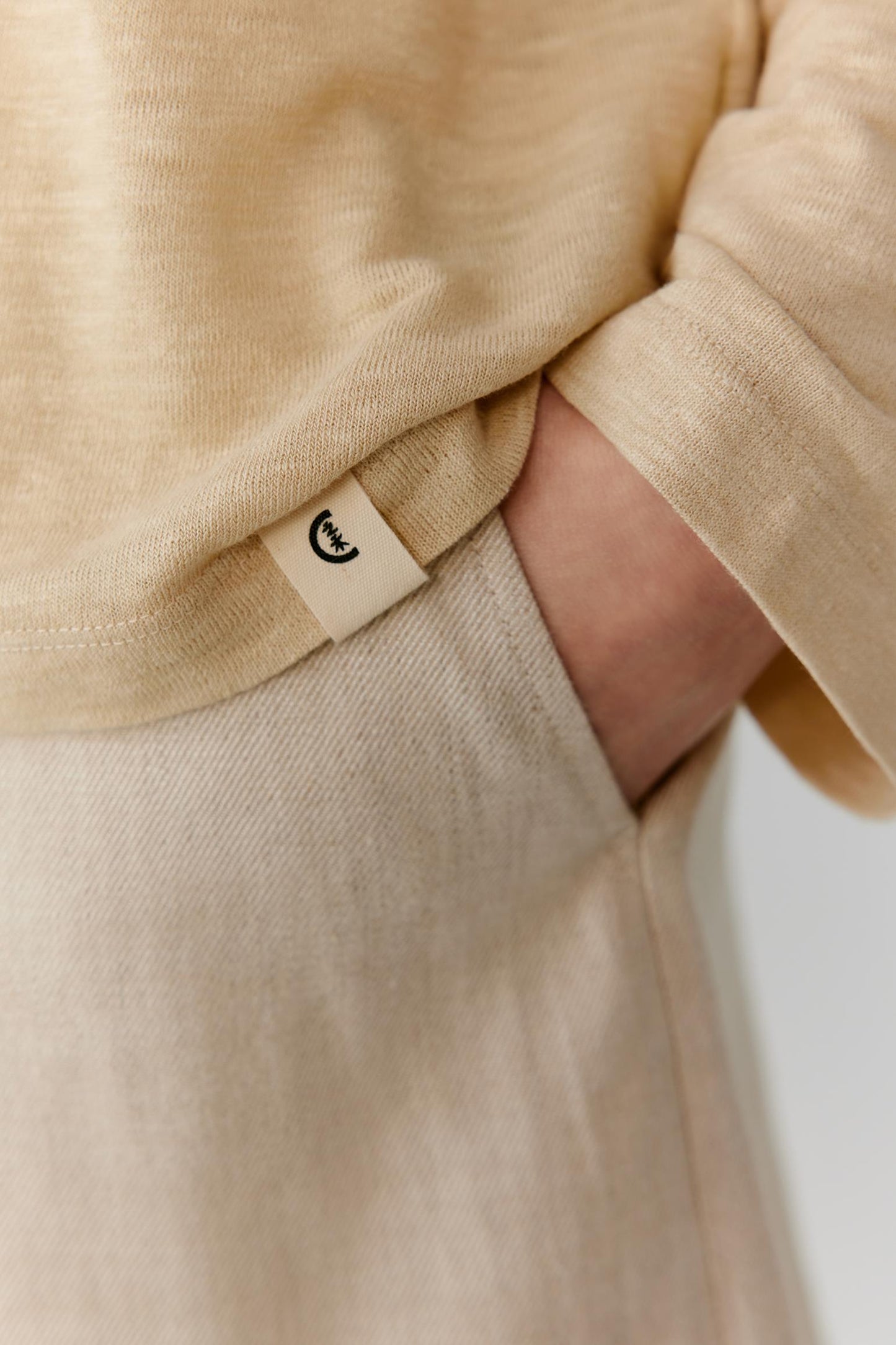Close-up of the lower sleeve and side hem showing the side slit, clean finishing and lightweight structure of the linen blend jersey. The image highlights the fluid drape, soft texture and understated construction details.