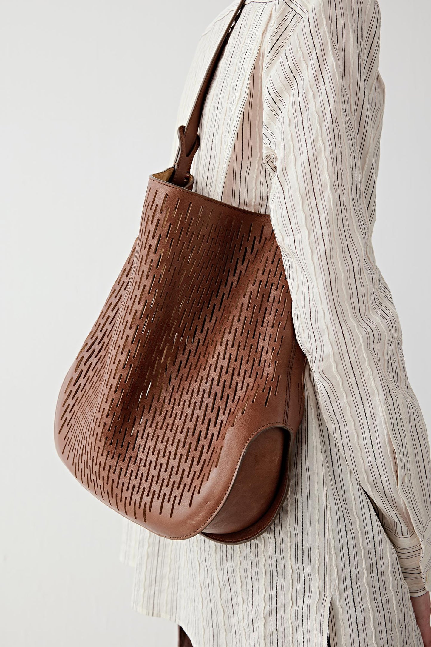 Close-up of the perforated dark brown leather surface and shoulder strap, highlighting the texture, graphic pattern and soft construction.