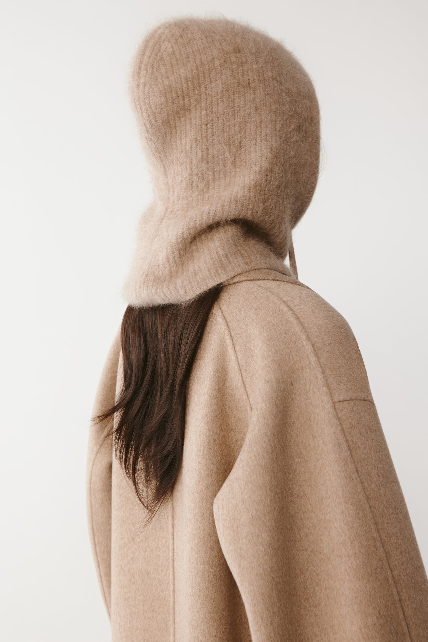 Back view of a beige knit hood with long drawstrings on a light background