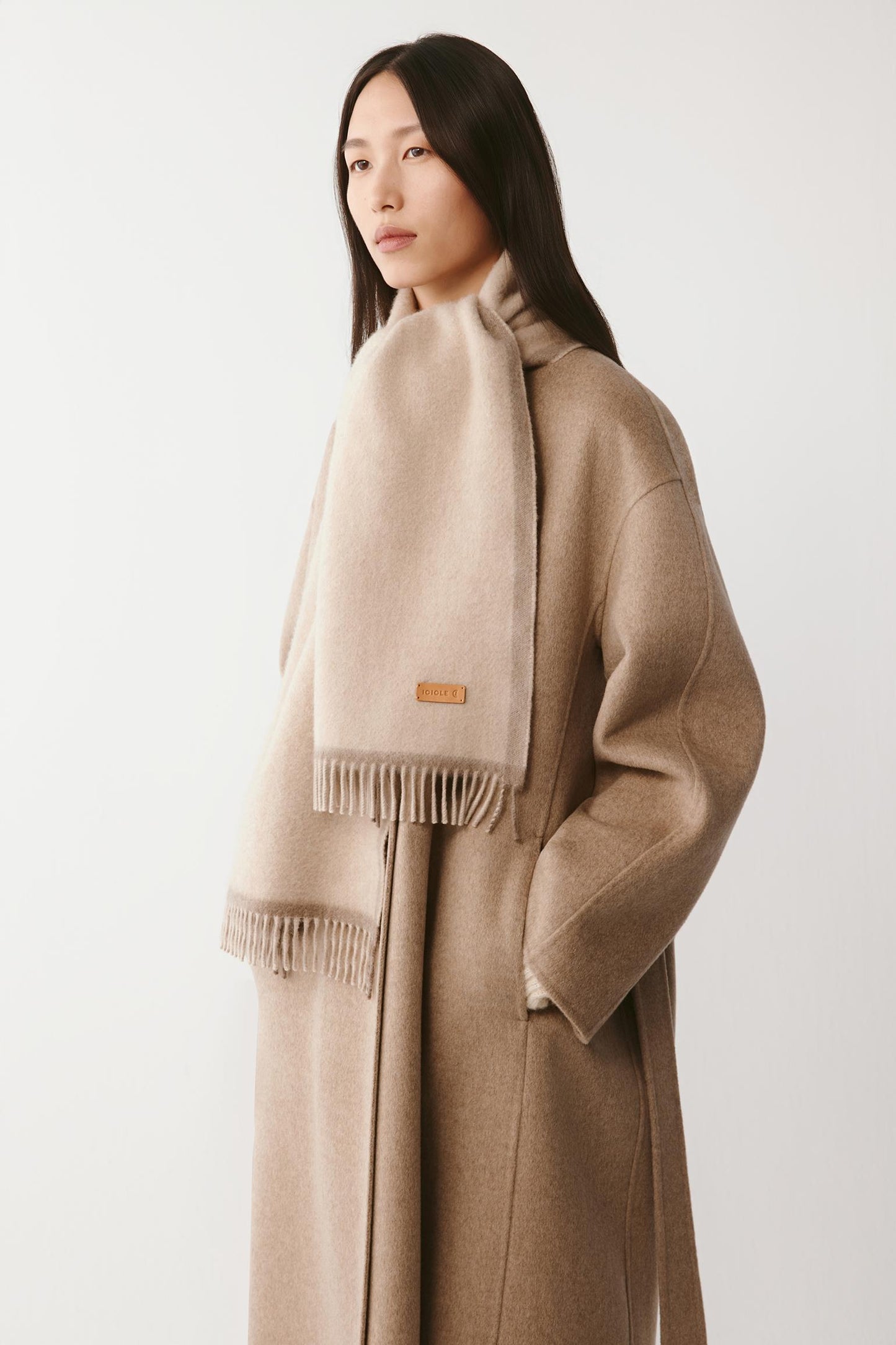 Full view of a woman wearing a cream wool scarf with fringed edges on a light background
