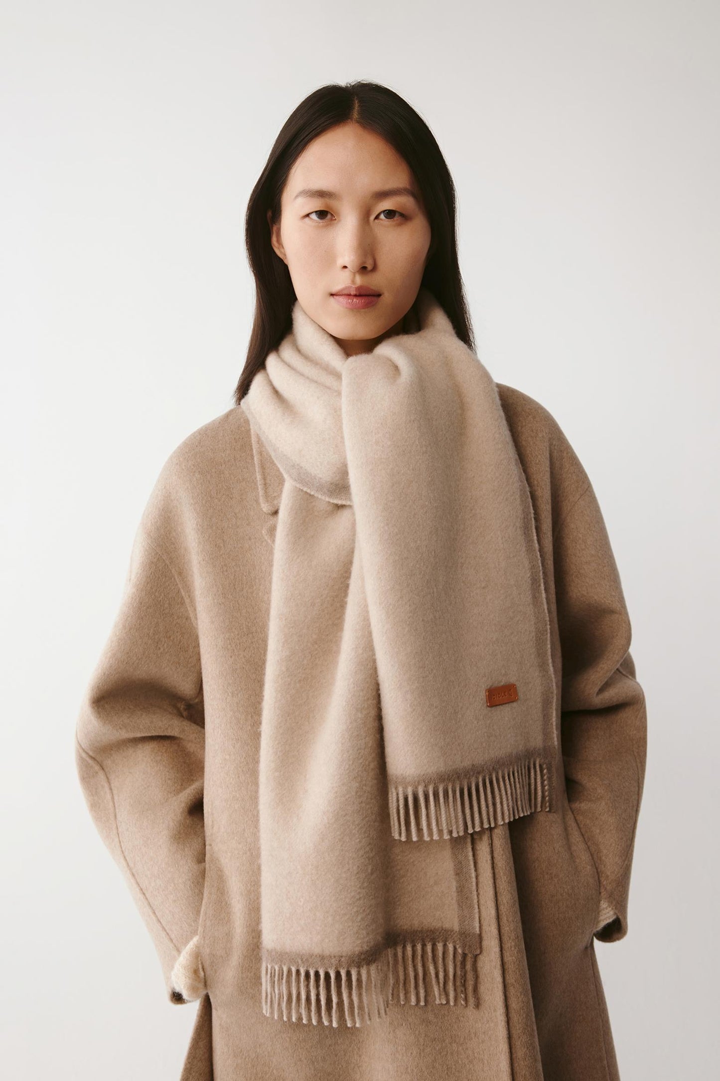 Woman wearing a large cream wool scarf styled with a beige coat on a light background