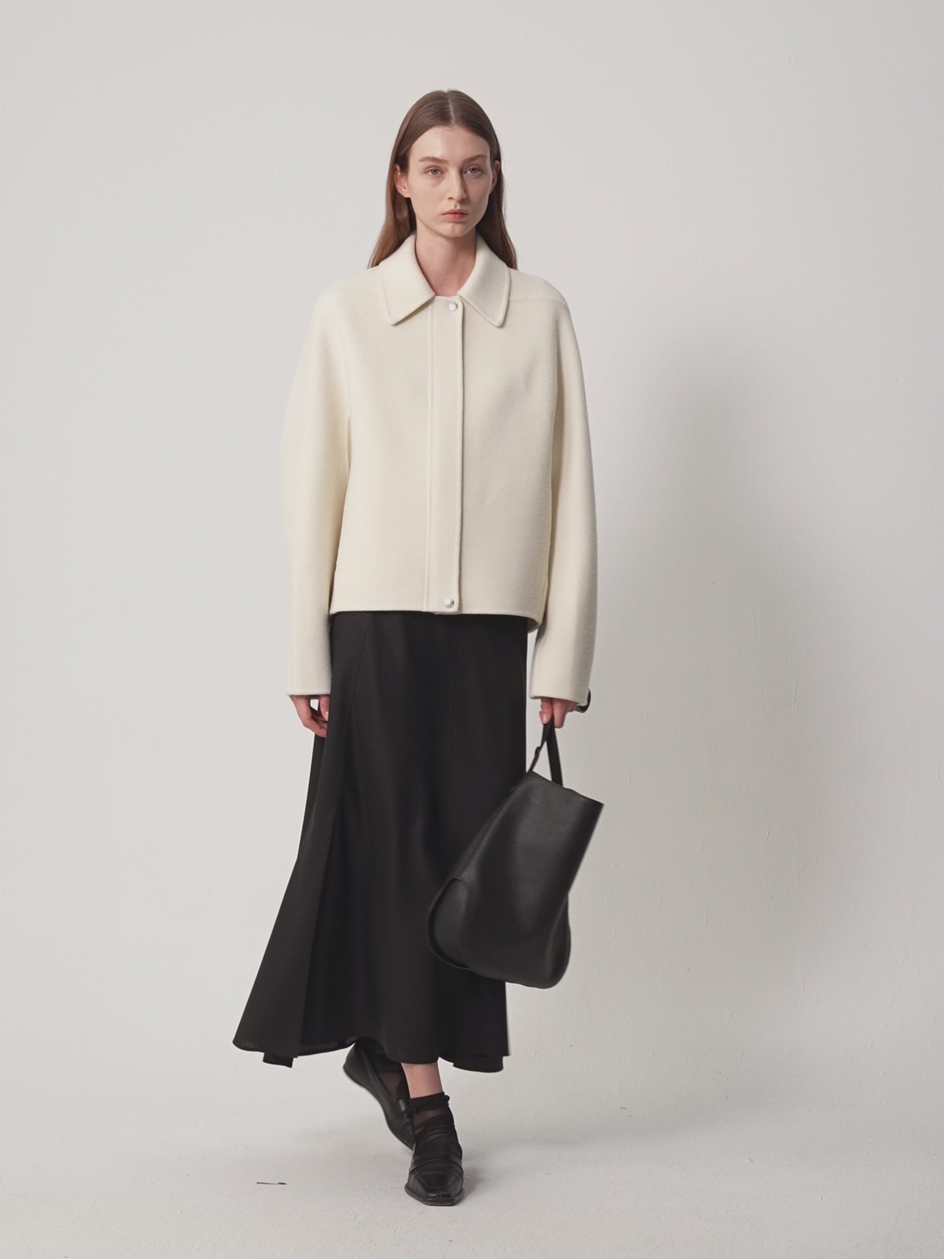 Video showing a woman wearing a cream-coloured double-sided wool and cashmere coat, paired with a black midi skirt and boots.
The model slowly turns to show the coat from different angles (front, side and back), revealing its long, flowing silhouette and natural, soft drape.
The movement highlights the coat's lightweight structure, the clean lines of the collar and the subtle texture of the undyed fabric.
