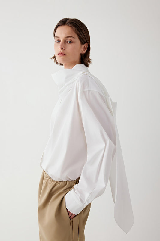 Video of a woman wearing the white cotton poplin shirt while turning slightly in a studio setting. The movement shows the fluid drape of the lightweight cotton fabric, the relaxed silhouette of the shirt and the way the long sleeves and hem move naturally with the body.