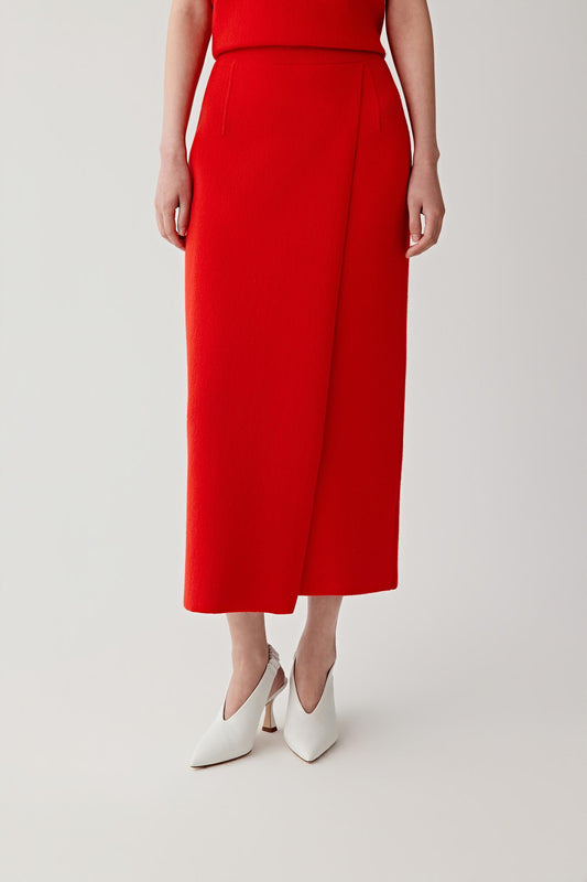 Video showing the model walking and turning while wearing the wool and cashmere skirt in intense red. The movement reveals the structured knit fabric and the steady drape of the garment as it moves with the body. The straight silhouette remains clean and balanced while the dense knit maintains its shape. The vibrant red tone stands out clearly as the fabric shifts with each step.