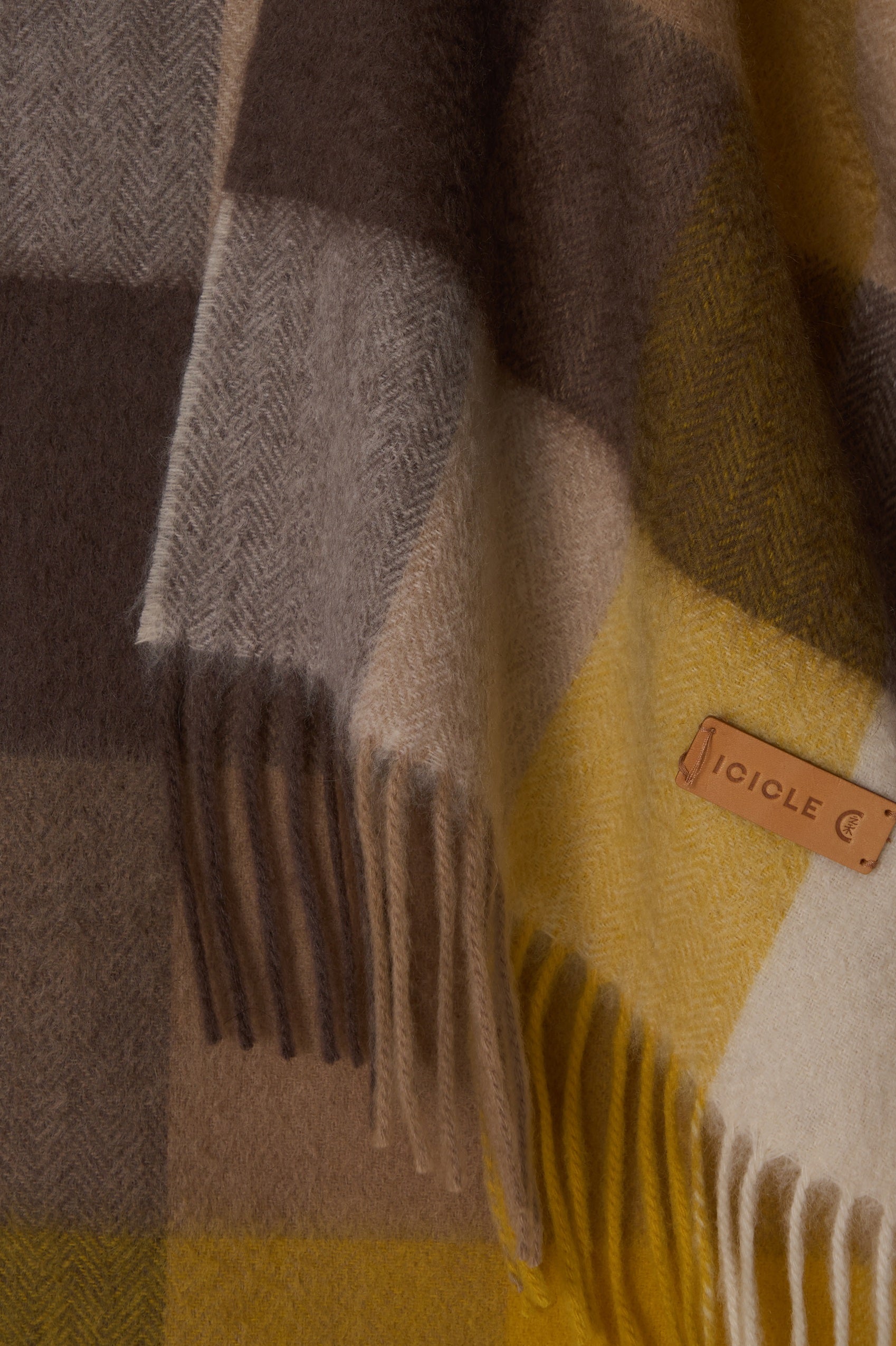 Plaid blanket with fringes and a visible brand label on a yellow background