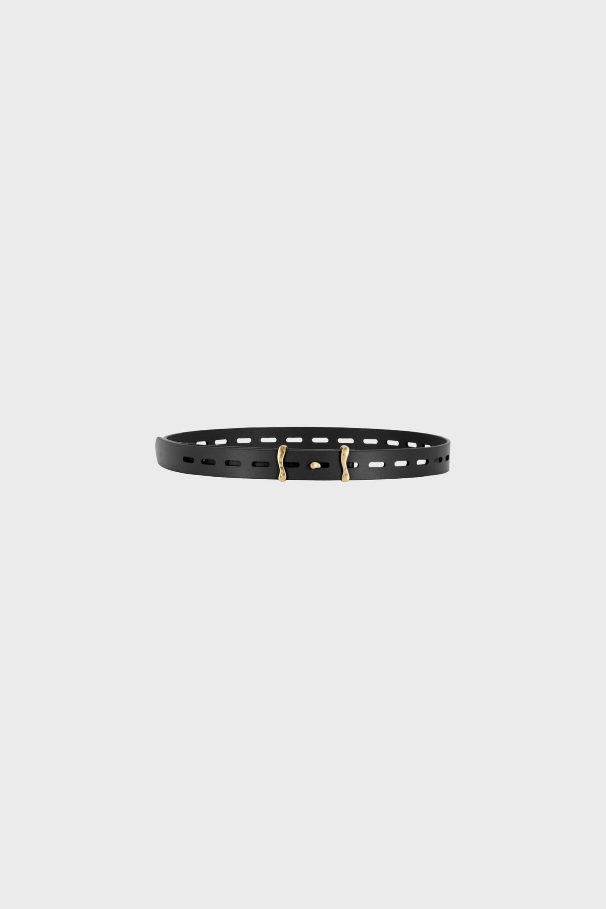 Flat lay product view of the slim black calf leather belt placed horizontally, showing the elongated perforations, smooth leather surface, precise edge finishing and sculptural brass buckle with a matte antique gold finish