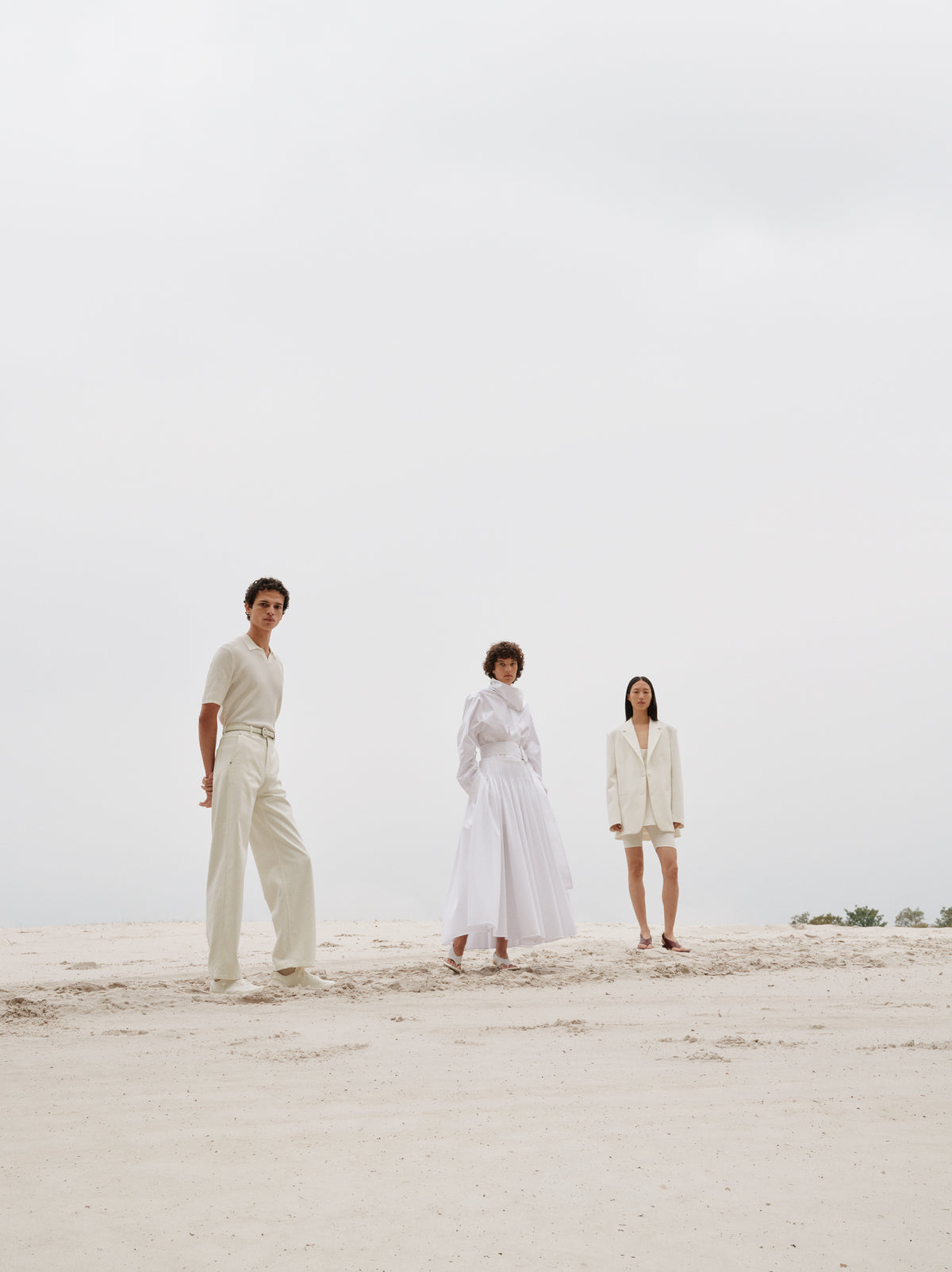 Three people in white outfits standing on a sandy beach with a clear sky.