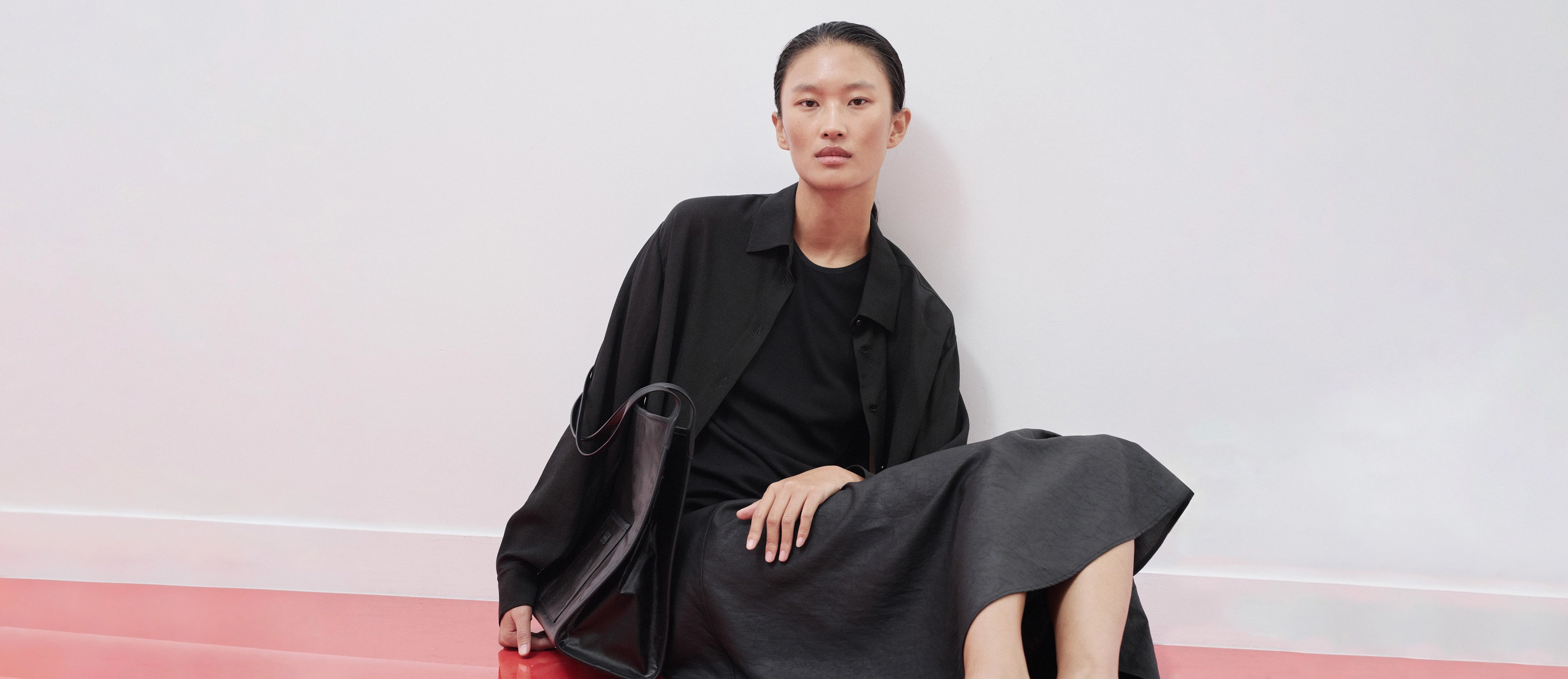 Woman in a black outfit sitting on a red carpet with a white background