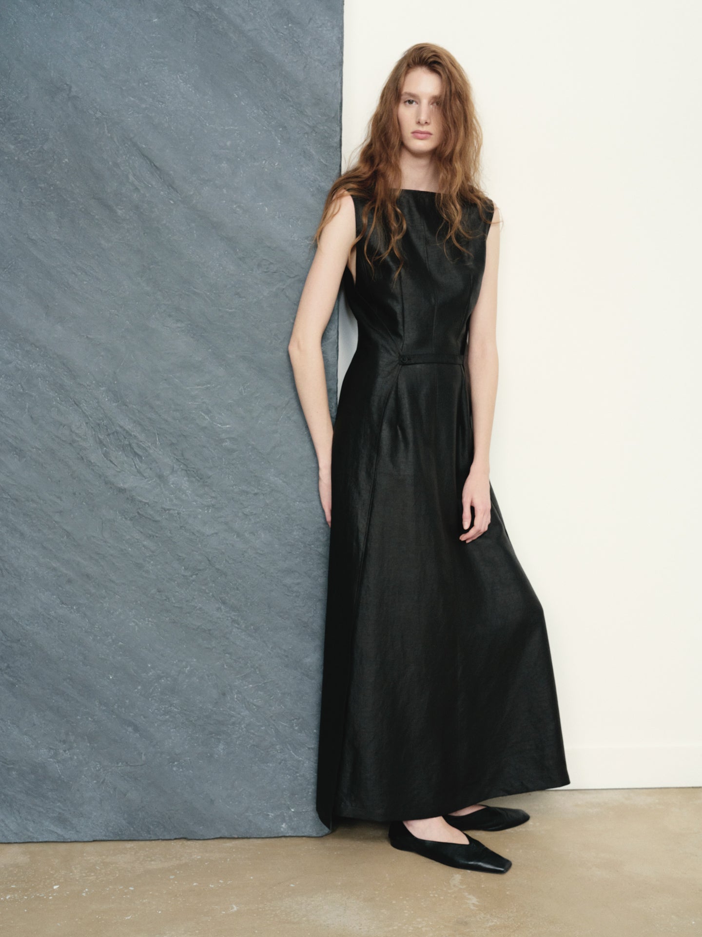 Woman wearing a black sleeveless dress against a plain wall.