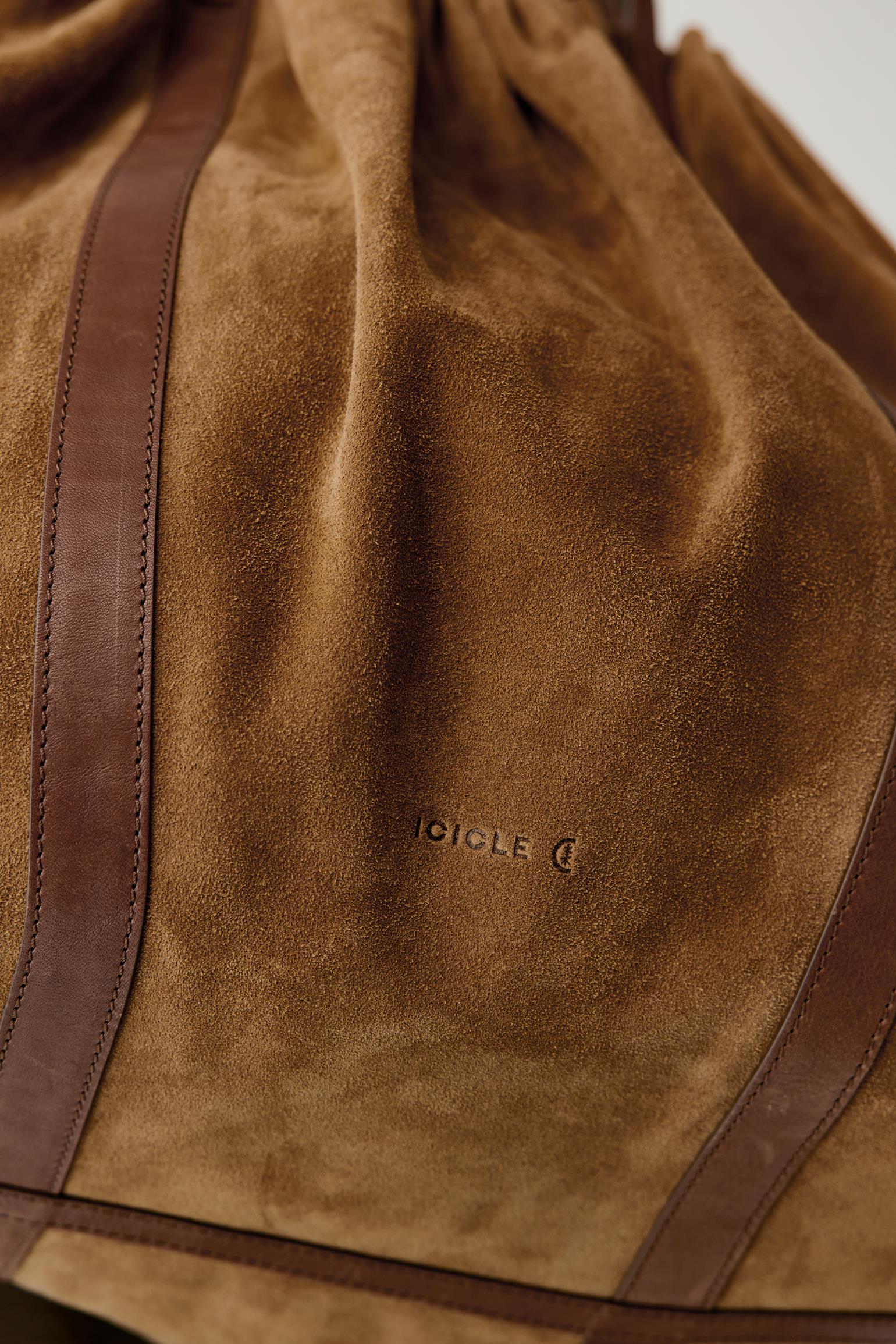 Close-up of a brown suede drawstring bag with dark brown leather trim and a debossed IDICLE logo on the front.