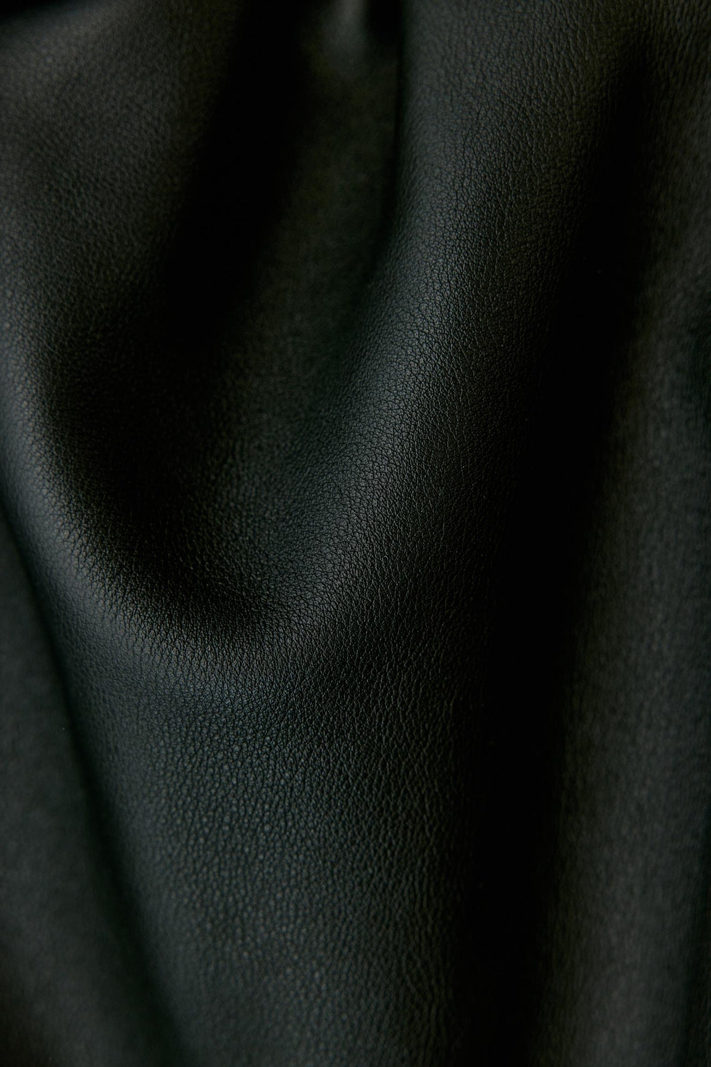A close-up of draped black textured leather fabric with soft folds and a pebbled surface.