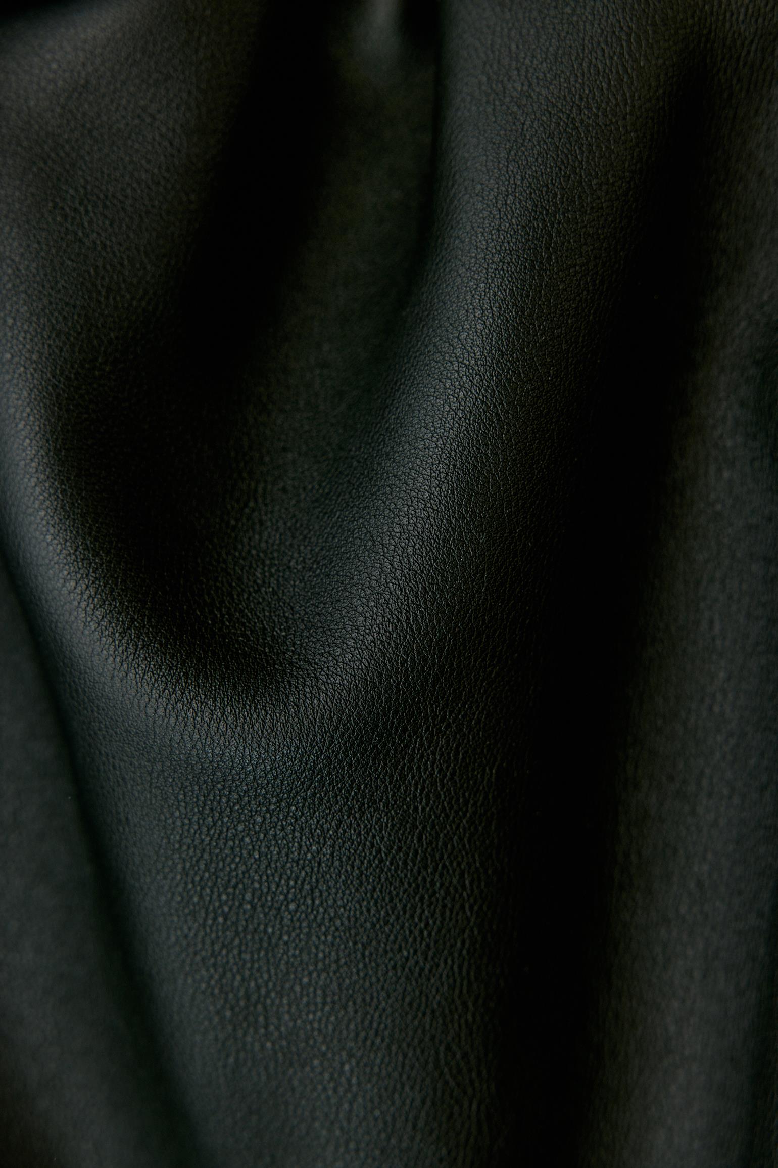 A close-up of draped black textured leather fabric with soft folds and a pebbled surface.