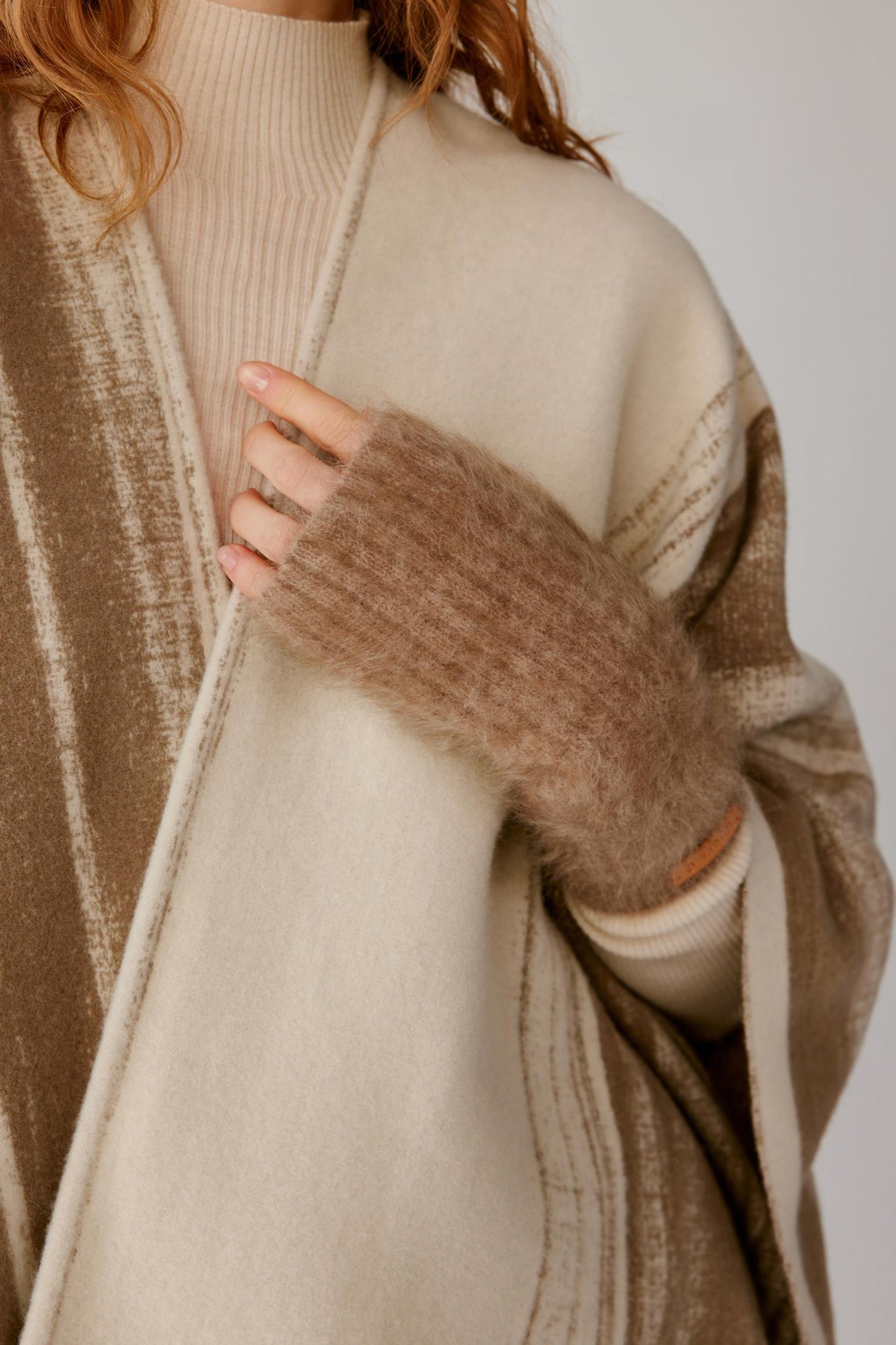 Front detail of a woman wearing natural taupe brushed cashmere fingerless gloves, highlighting the ribbed knit texture and elongated shape.