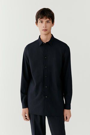 Man wearing a dark navy silk-and-wool check shirt with a relaxed straight fit, front portrait view highlighting the classic collar and subtle check pattern.