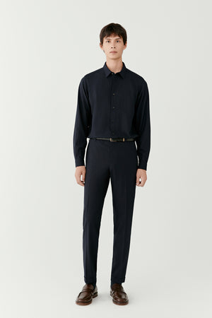 Man wearing navy check trousers in a wool and silk blend with a tailored straight fit, styled with a navy shirt, full-length front view.