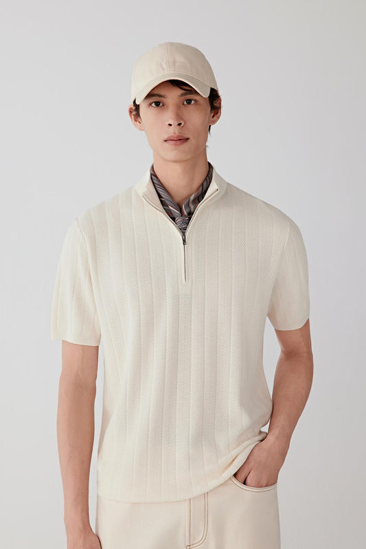 Front view of a cream silk-yarn pullover worn with dark trousers, highlighting the smooth knit surface, short sleeves and relaxed, straight silhouette.