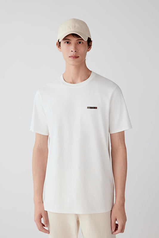 Full-length front view of a white cotton jersey T-shirt worn with light trousers, showing a straight fit and clean neckline.