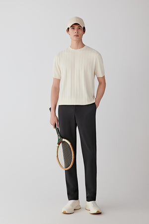 Man wearing dark grey wool jersey straight-leg trousers with a relaxed fit, styled with a light beige T-shirt and beige cap, full-length front view.