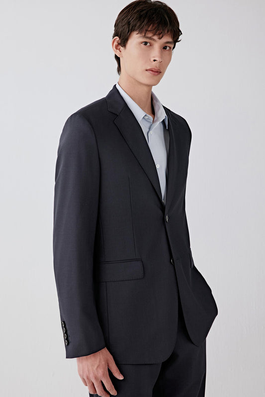 Man wearing a deep black twist wool jacket with a tailored straight cut and notched lapel, styled with matching trousers and a light shirt; front three-quarter view showing the clean lines, structured shoulders and smooth drape.