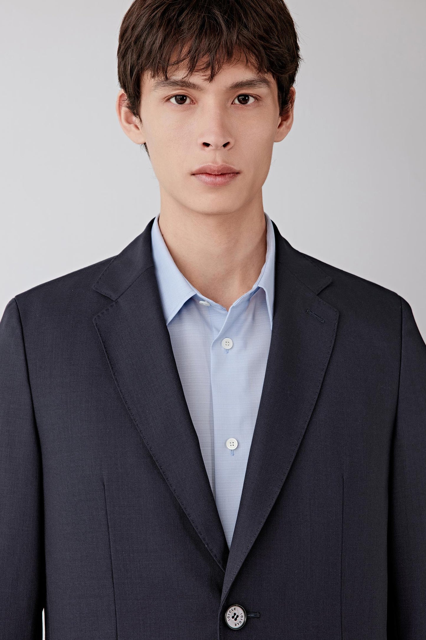 Close-up of the lapel and upper chest, revealing the fine woven texture, matte finish and precise tailoring of the collar.