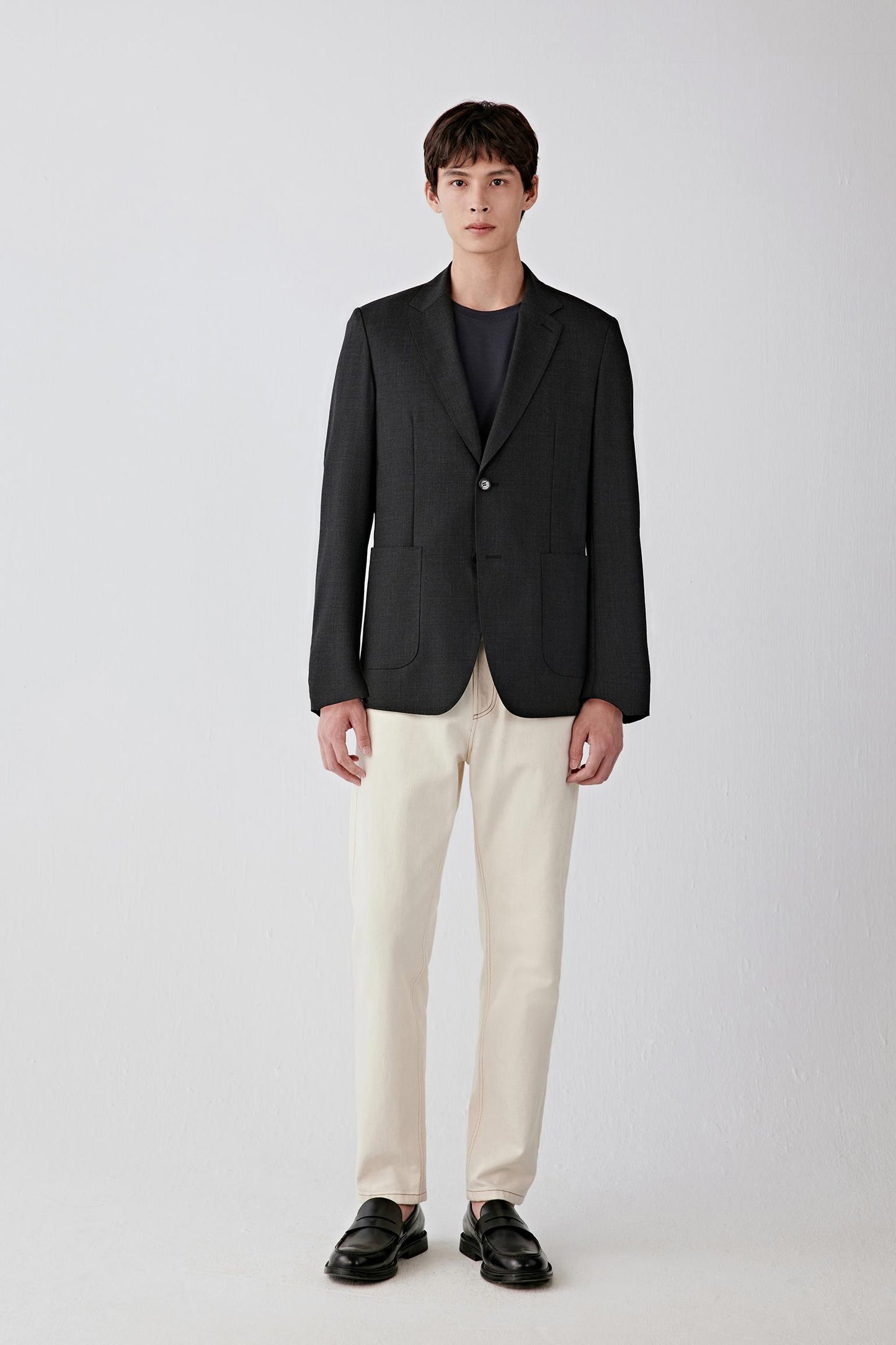 Full-length front view highlighting the single-breasted closure, straight silhouette and contrast between the dark jacket and light trousers, with a balanced, slightly fitted cut through the torso.