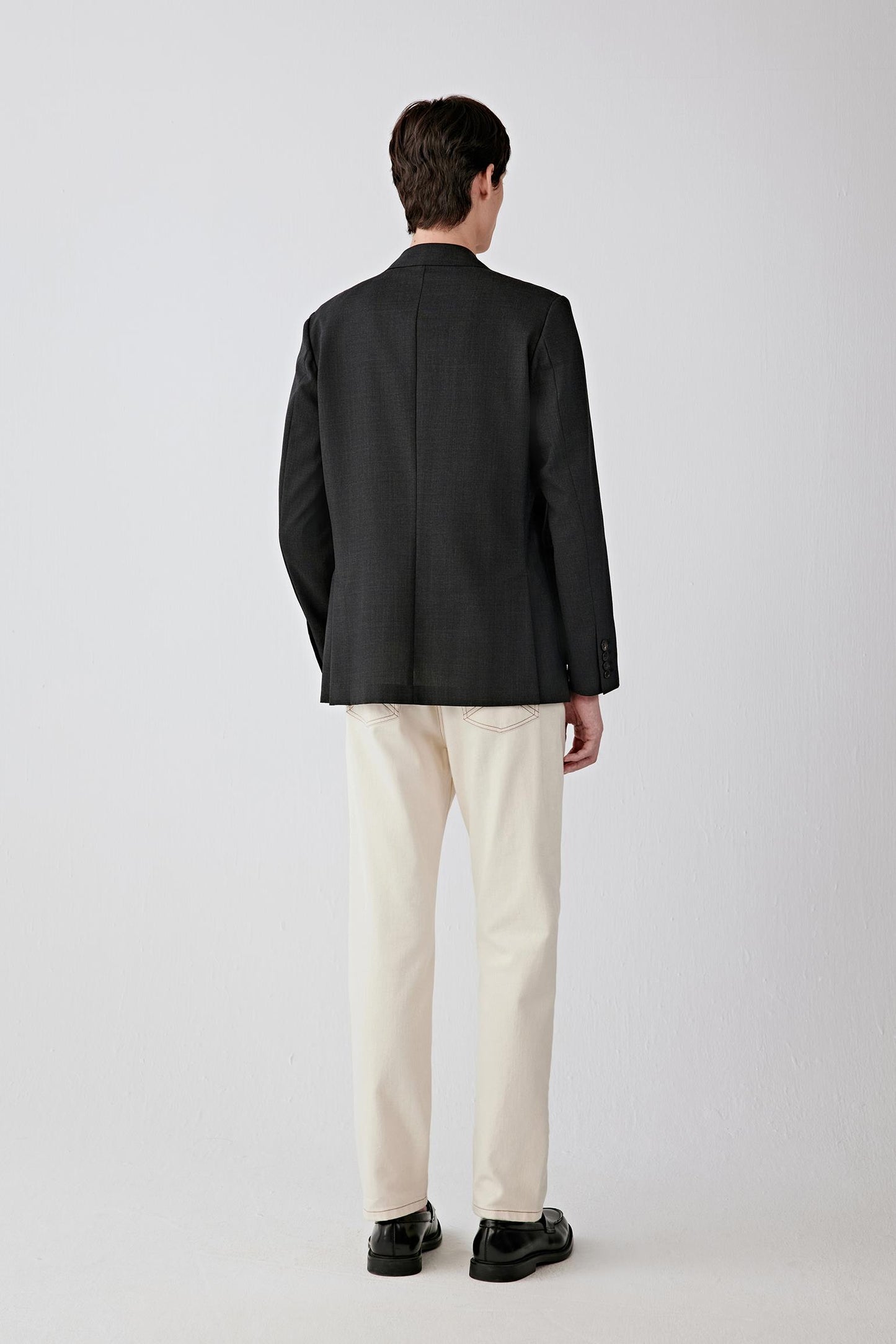 Back view showing the clean shoulder line, straight fall from upper back to hem and minimal construction, emphasizing the refined, structured drape.