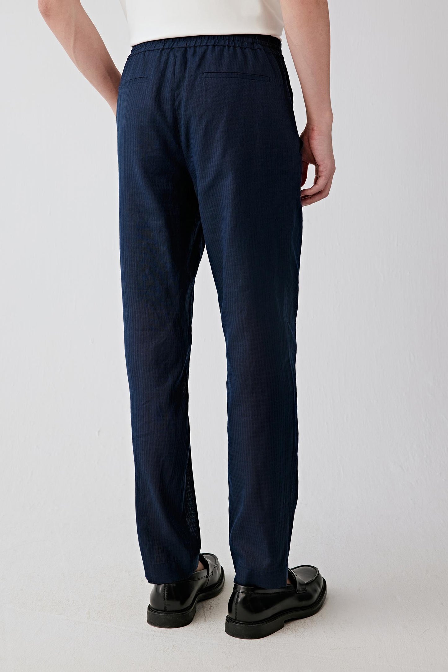 Back view emphasizing the fluid fall of the fabric and the clean straight-leg silhouette. The subtle checked surface introduces tonal depth and understated texture.