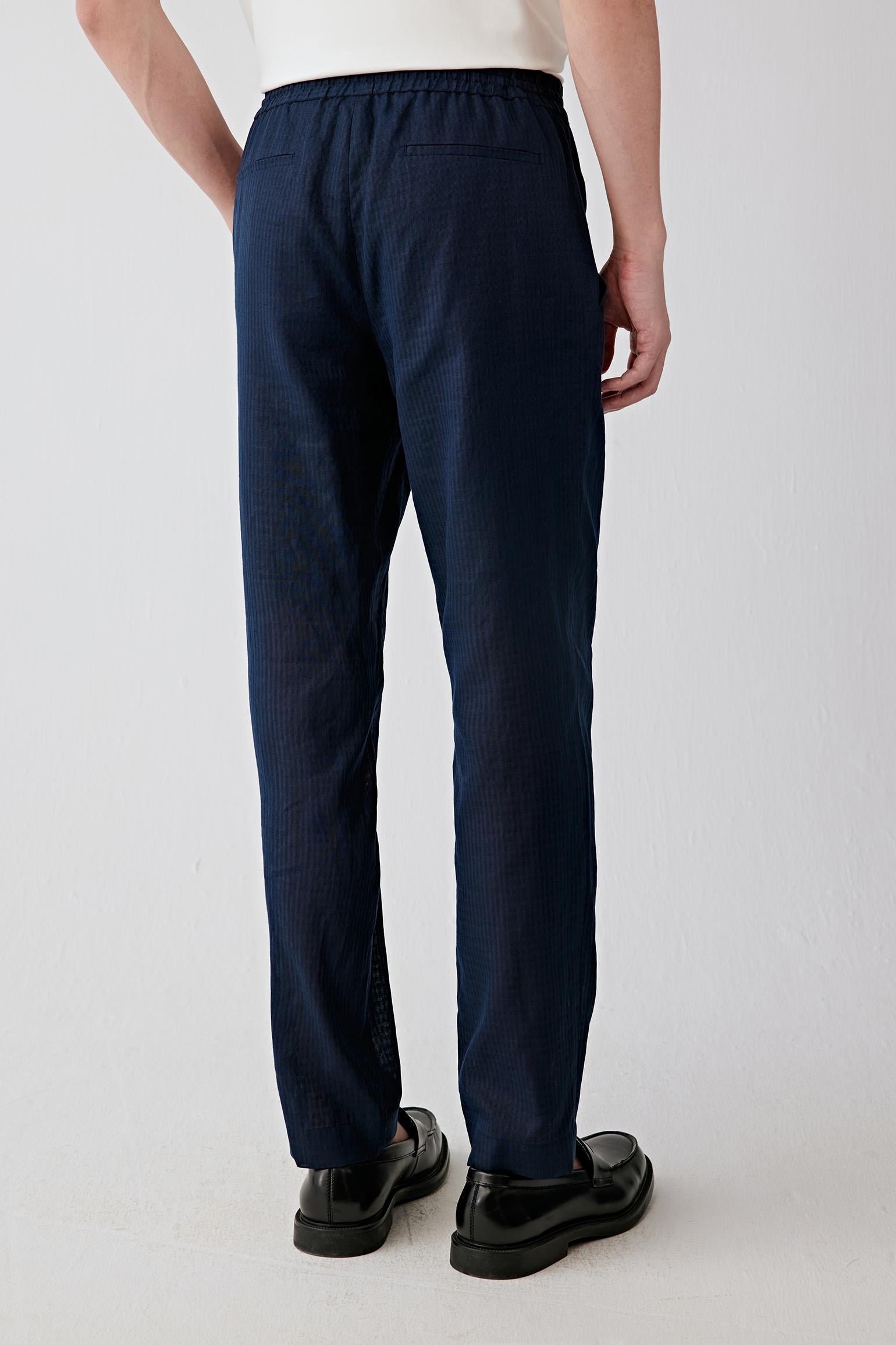 Back view emphasizing the fluid fall of the fabric and the clean straight-leg silhouette. The subtle checked surface introduces tonal depth and understated texture.
