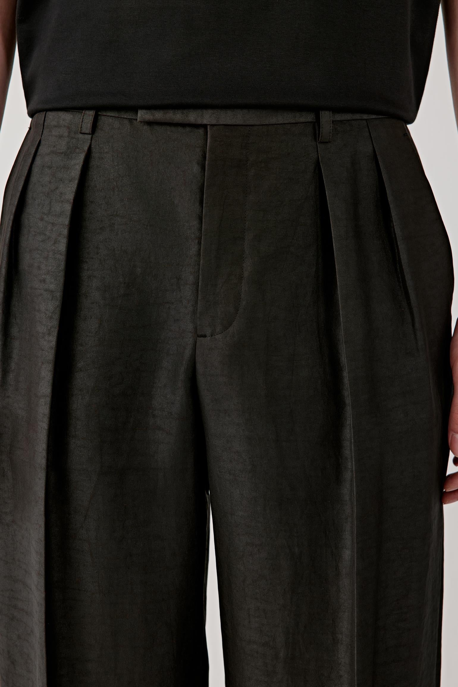 Close-up of the waist area, showing front pleats, waistband construction and subtle texture of the fabric.