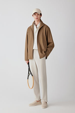 Front view of a male model wearing a warm brown jacket crafted from worsted wool blended with silk, styled with a light cap, cream trousers and neutral shoes.