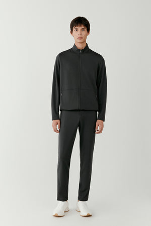 Man wearing anthracite wool jersey straight-leg trousers with a relaxed tailored fit, styled with a matching anthracite zip jacket, full-length front view.