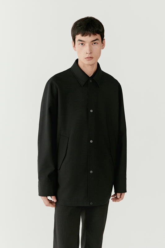 Three-quarter front view highlighting the concealed button placket and tailored collar of the black wool and silk jacket.