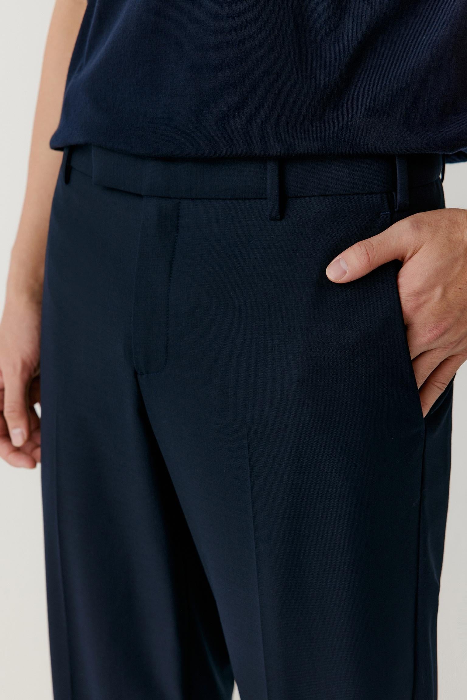Close-up of a person wearing dark navy trousers with a matching belt, paired with a navy top, against a light neutral background.